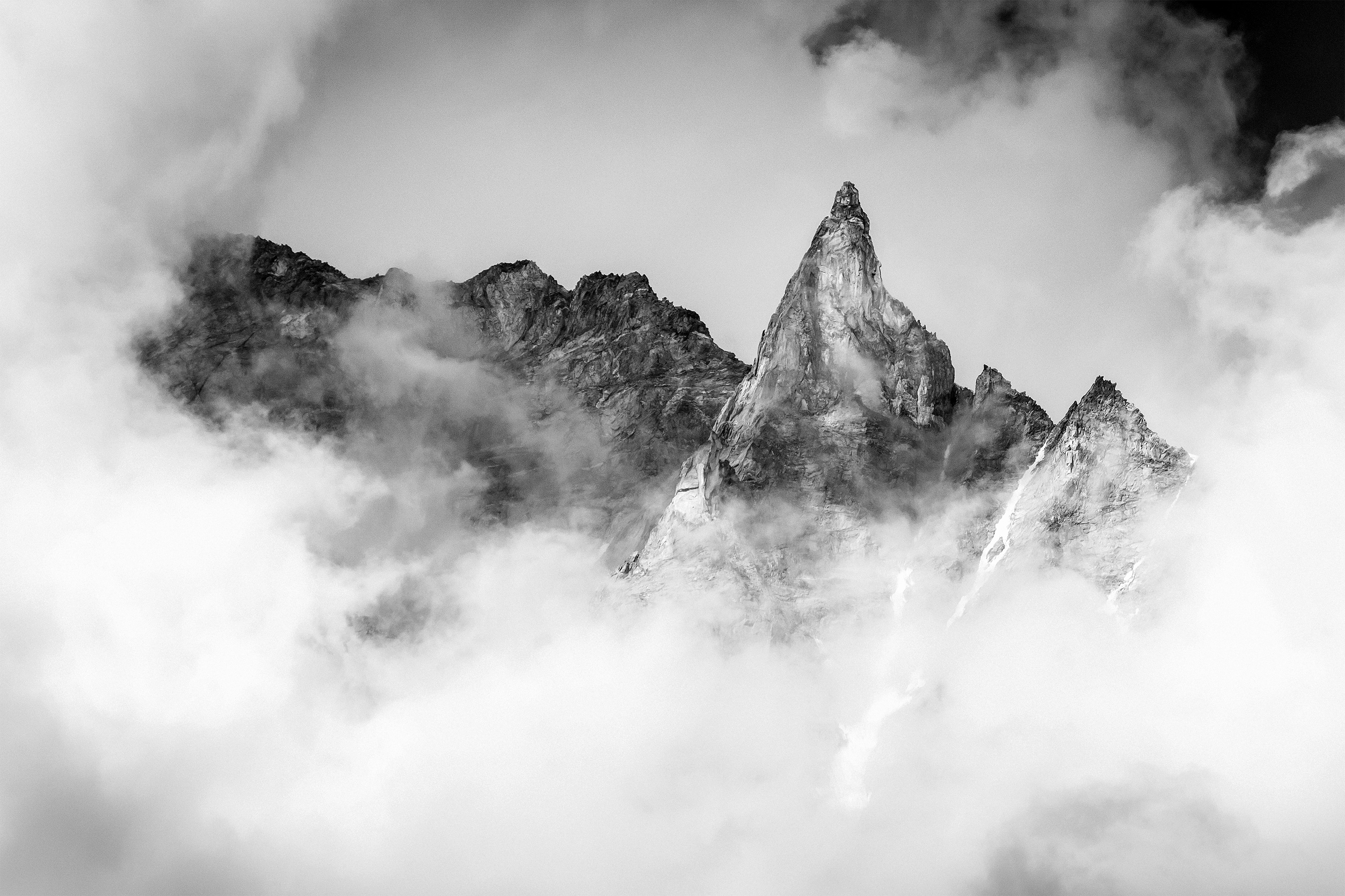 Jagged mountain peaks emerge from swirling clouds HD Wallpaper