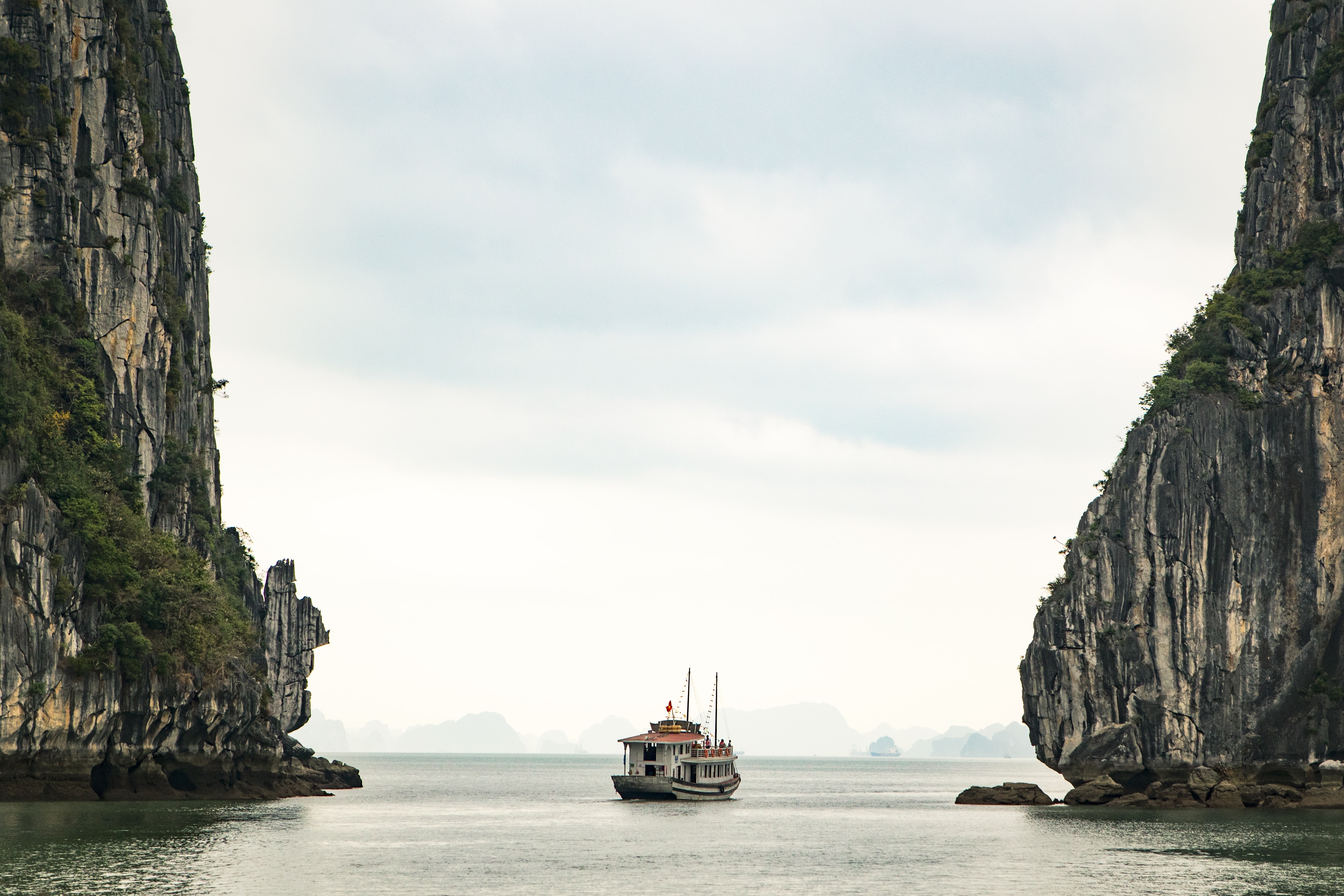Boat sailing between limestone karsts in Ha Long Bay HD Wallpaper
