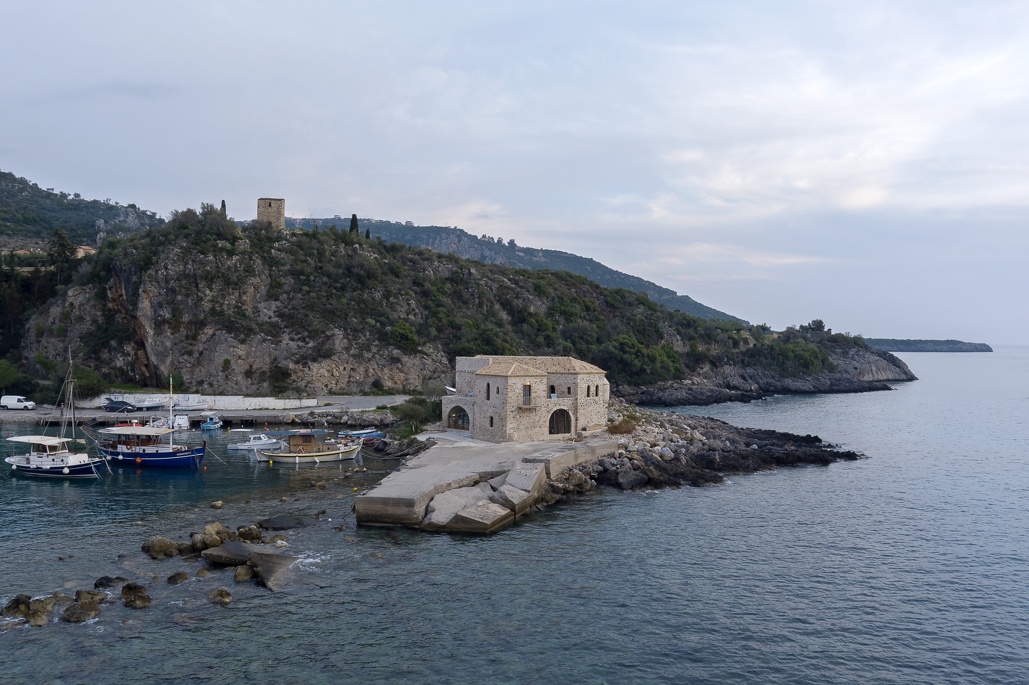 Stone building on a rocky peninsula in a harbor with boats HD Wallpaper