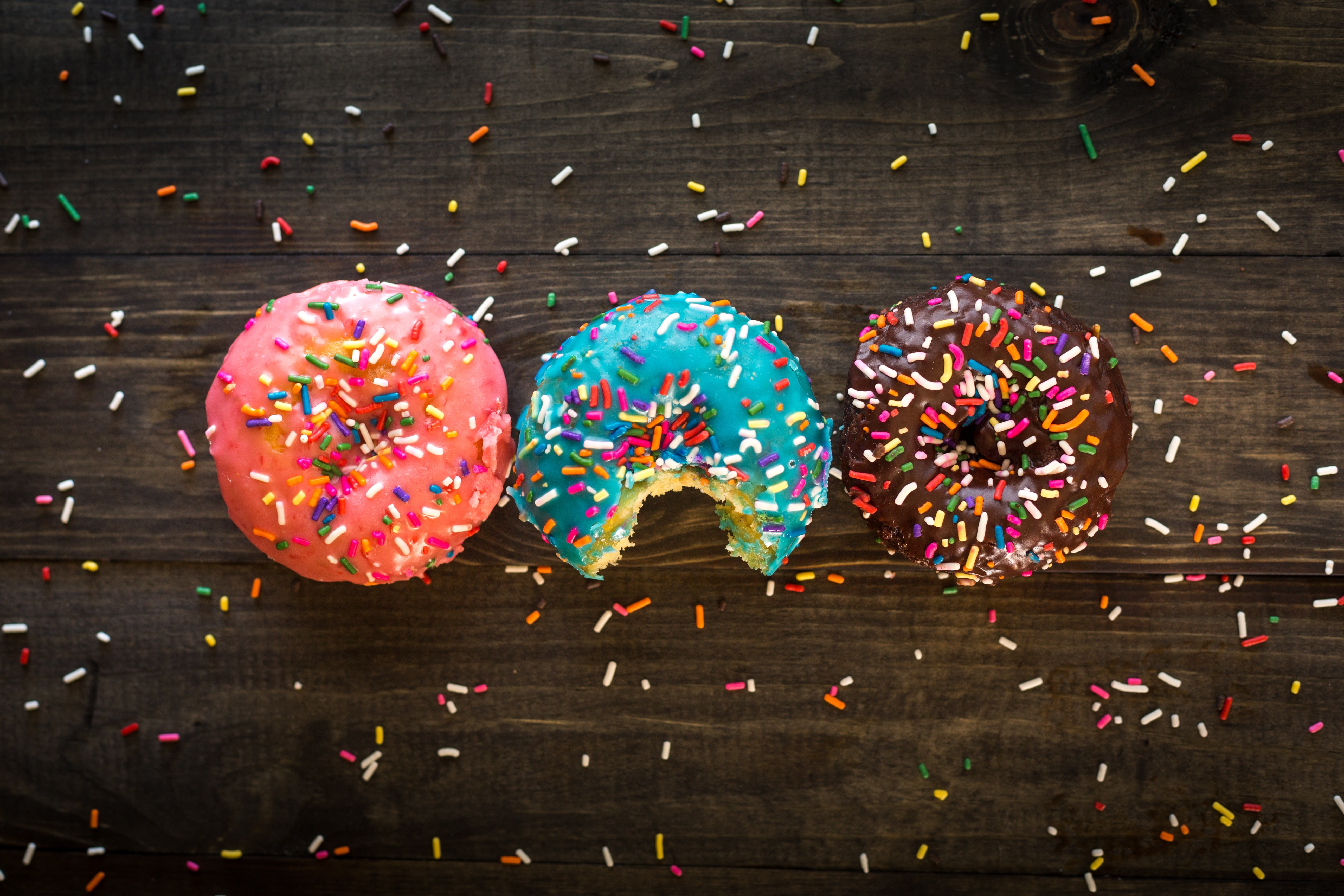 Three donuts with sprinkles on a wooden surface HD Wallpaper