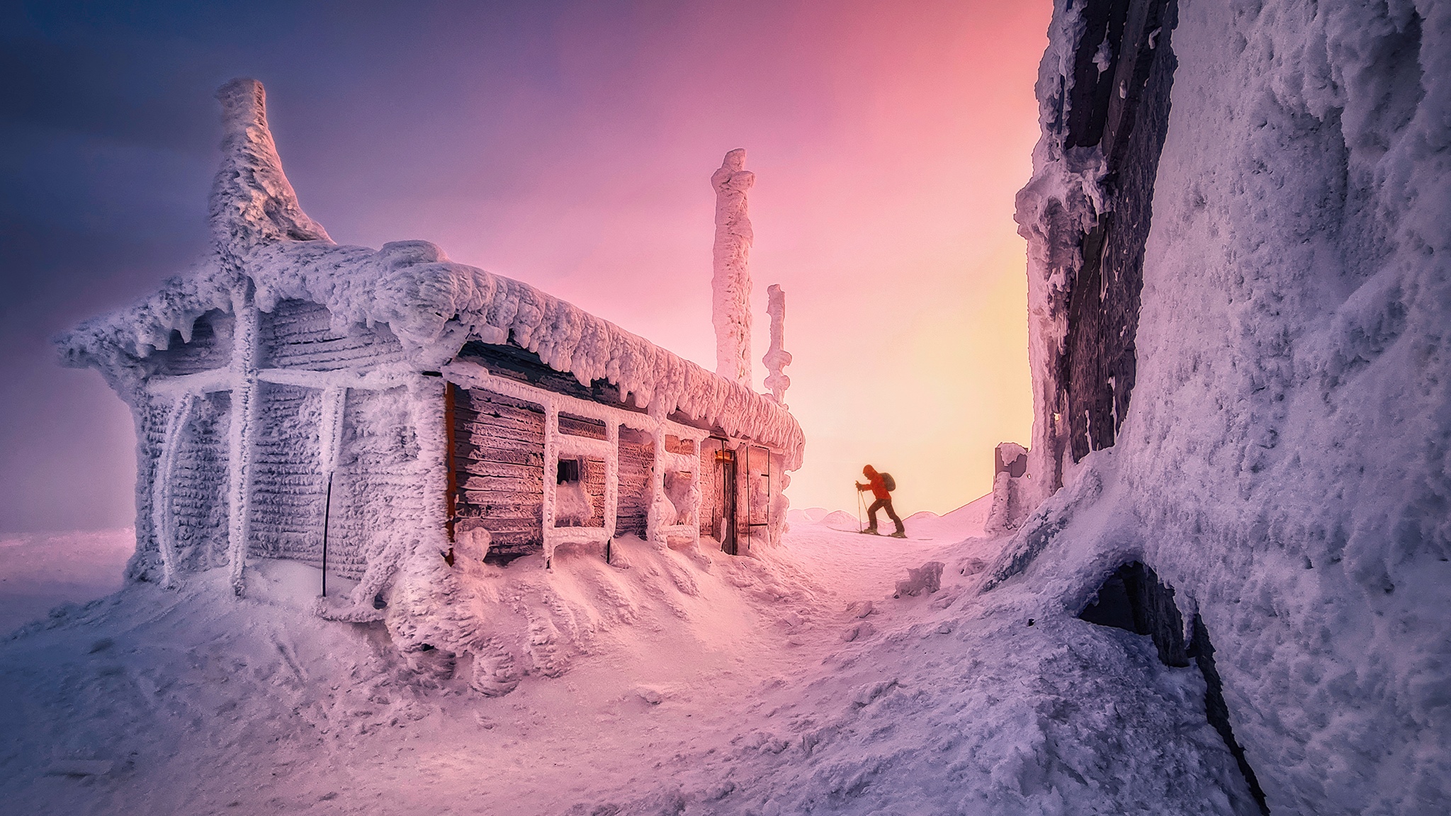 Snow covered cabin in winter with a skier HD Wallpaper