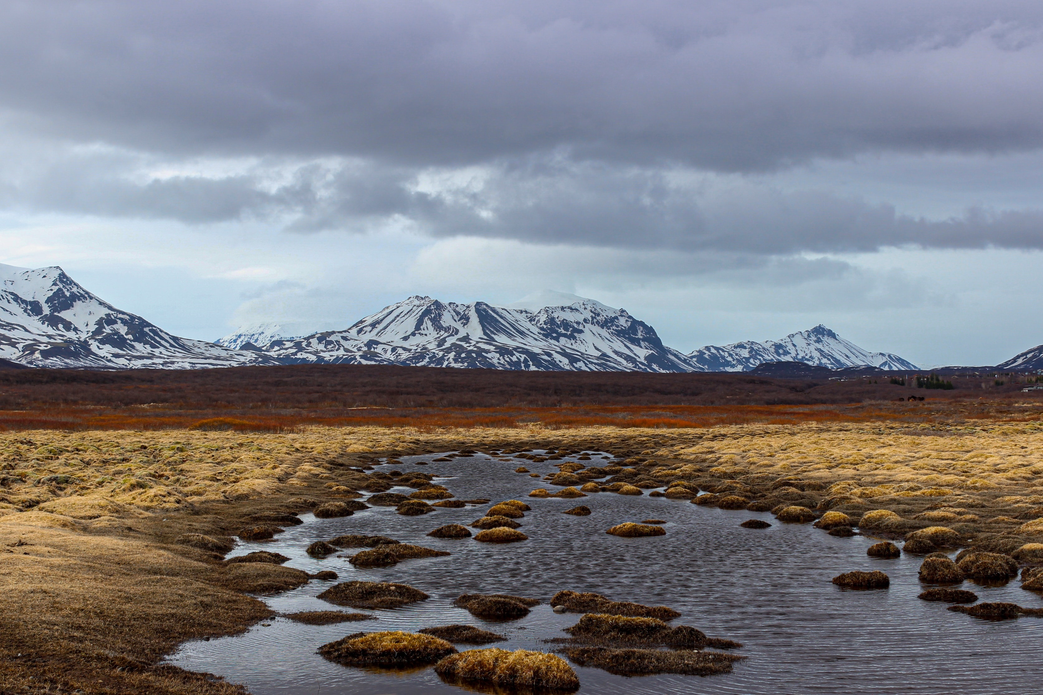 Snow-capped mountains over a marshy landscape with a river HD Wallpaper