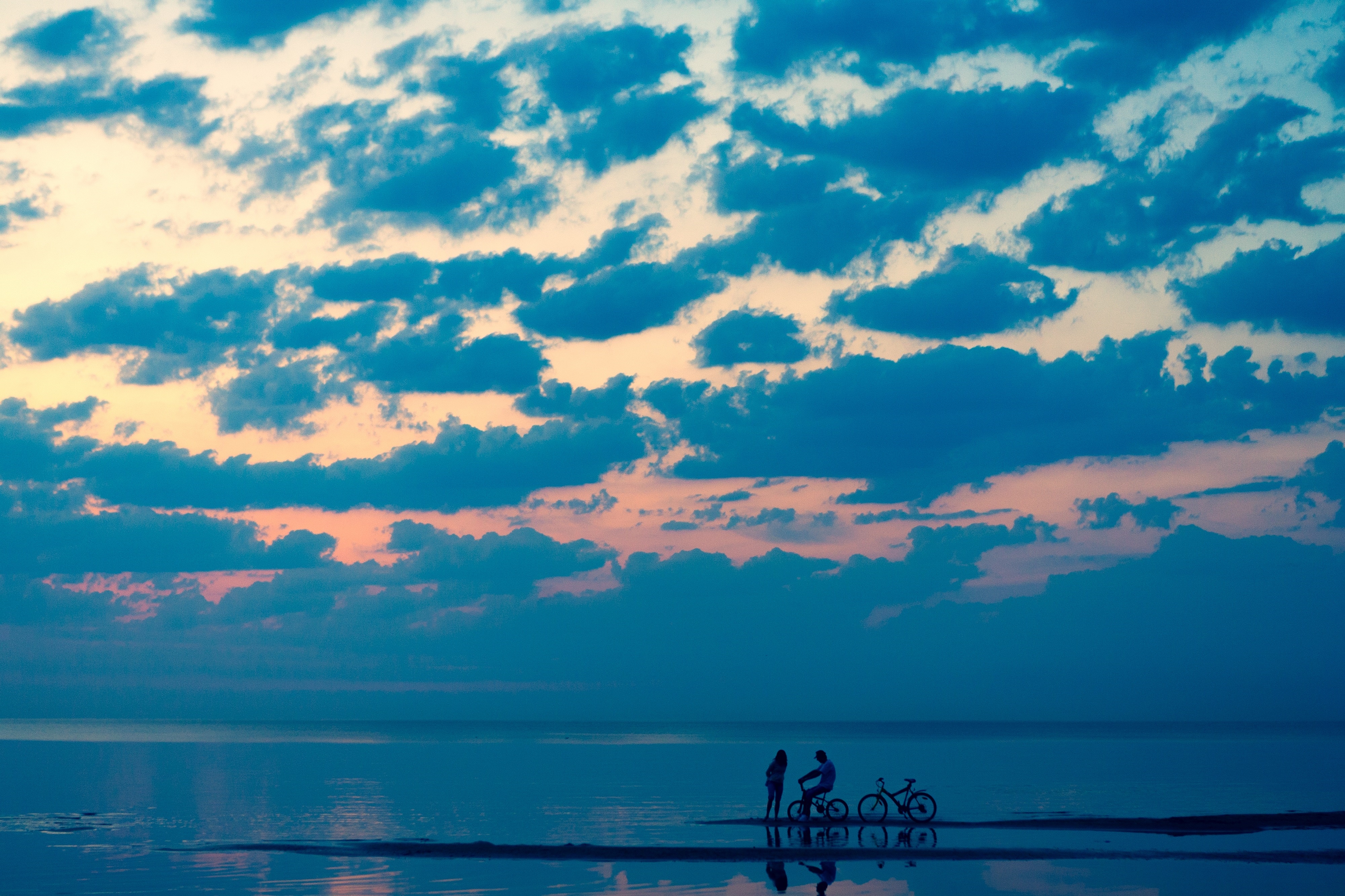 Couple with bicycles on a beach at sunset HD Wallpaper