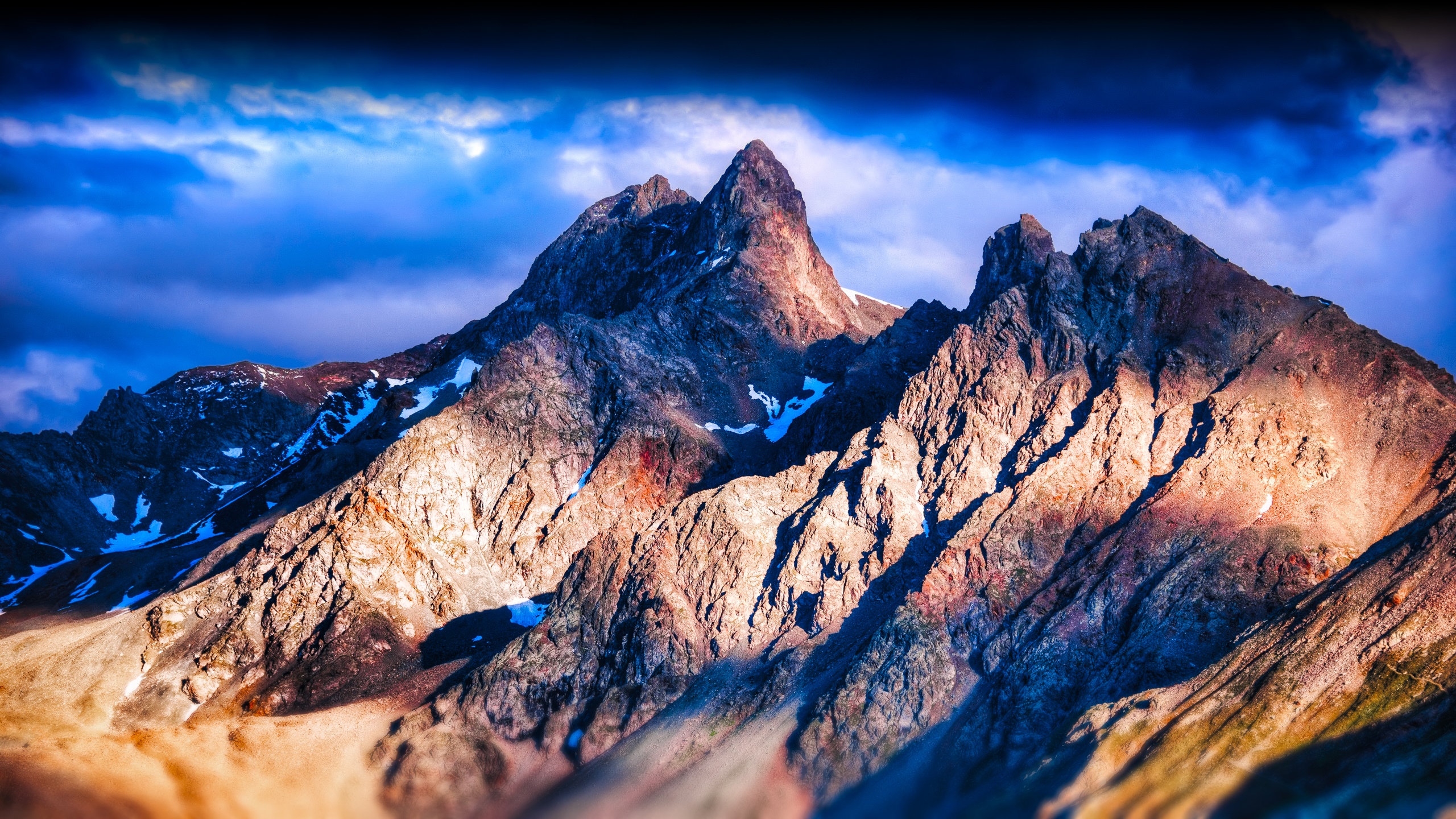 Jagged mountain peaks under a dramatic blue sky HD Wallpaper