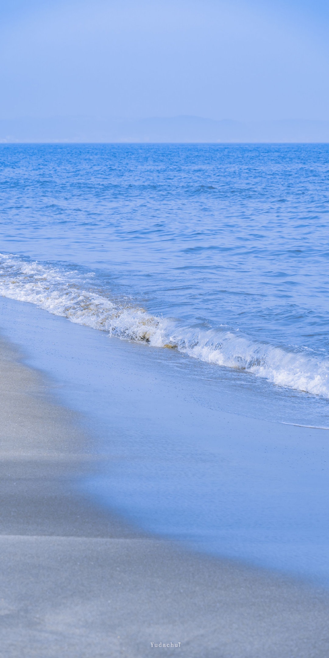 Gentle waves lap onto a sandy beach under a clear sky. HD Phone Wallpaper