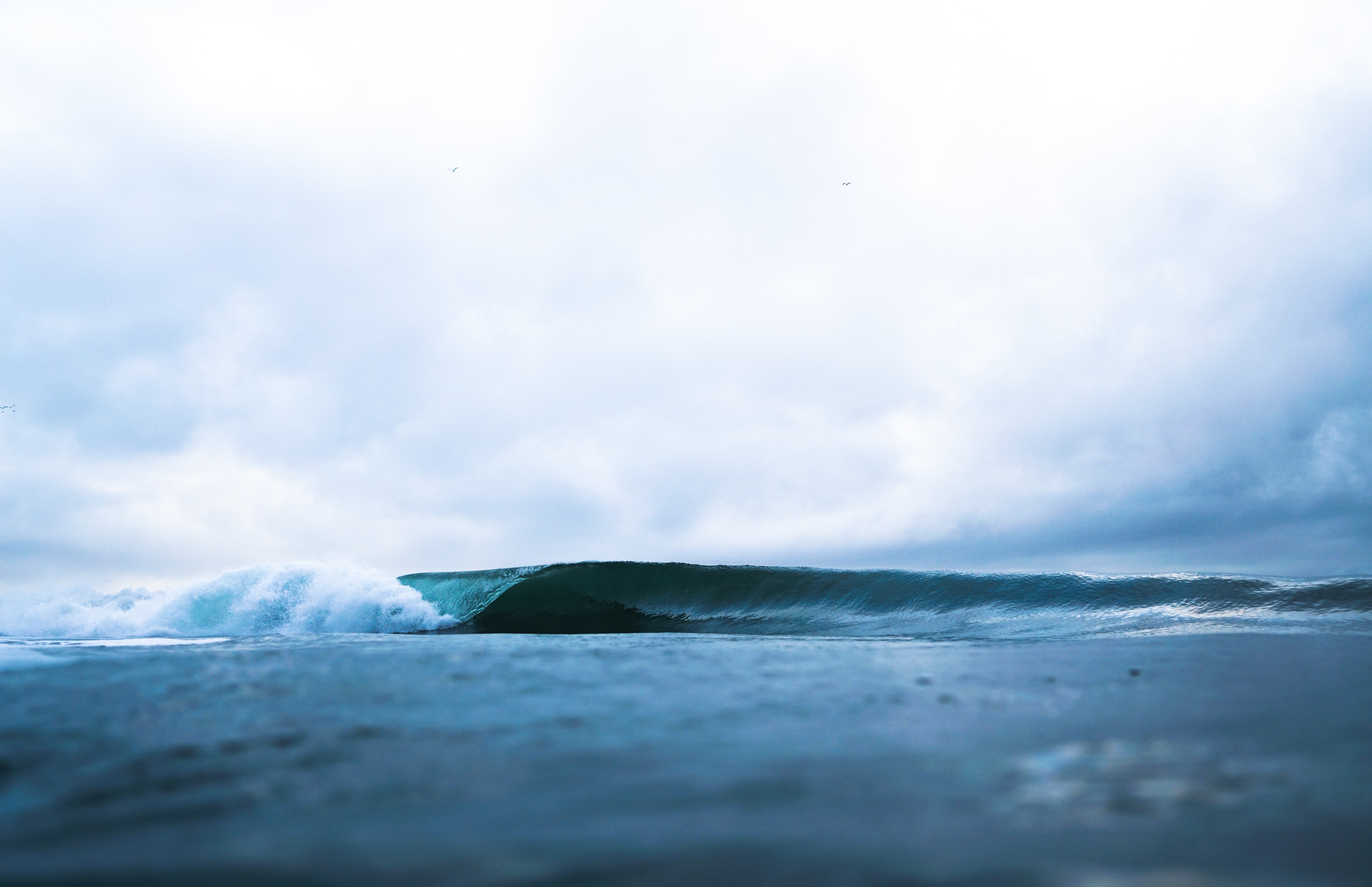 Ocean wave breaking under a cloudy sky HD Wallpaper
