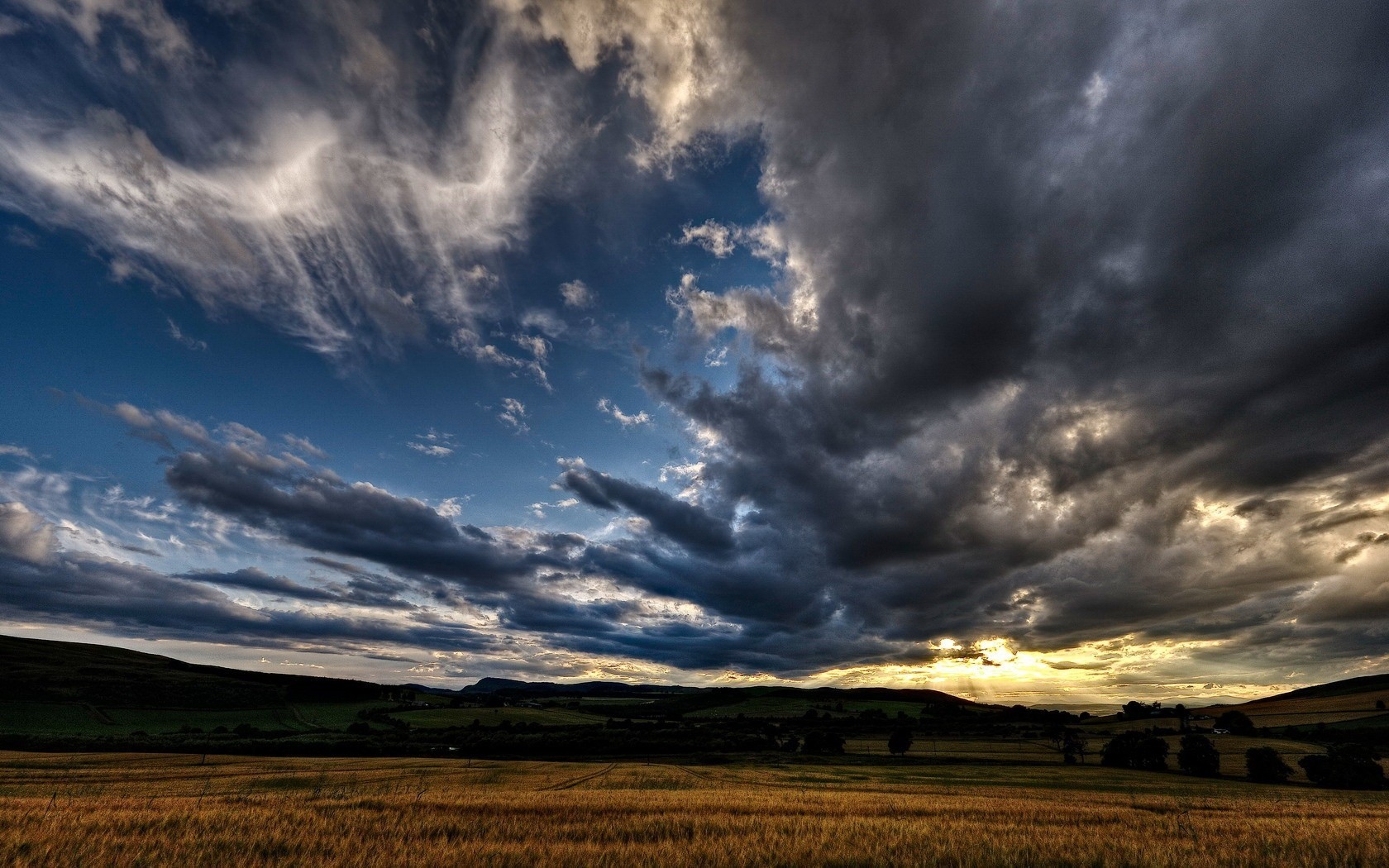 Dramatic clouds over a golden field and rolling hills HD Wallpaper