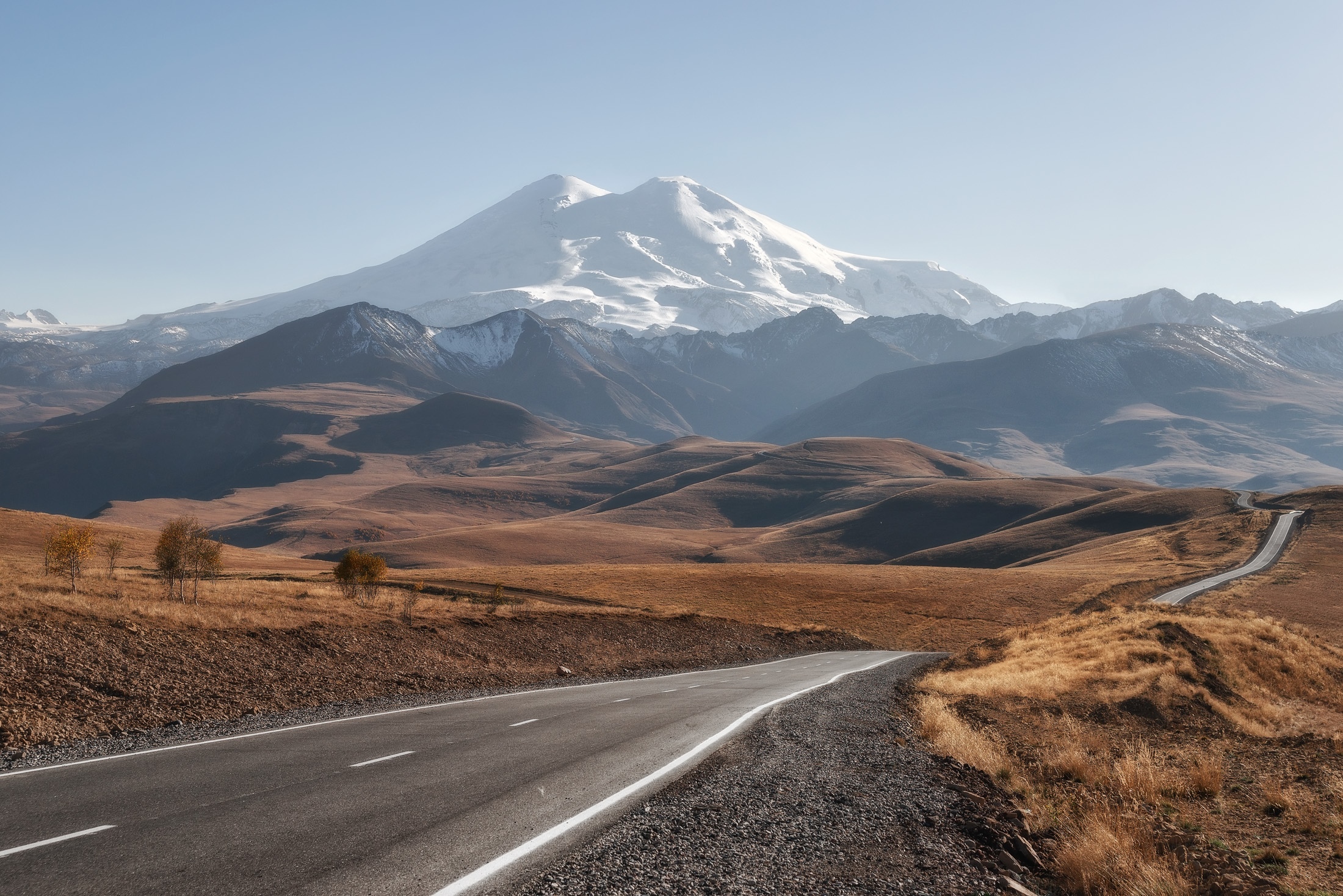 Road leading to snow-capped mountains under a clear sky HD Wallpaper