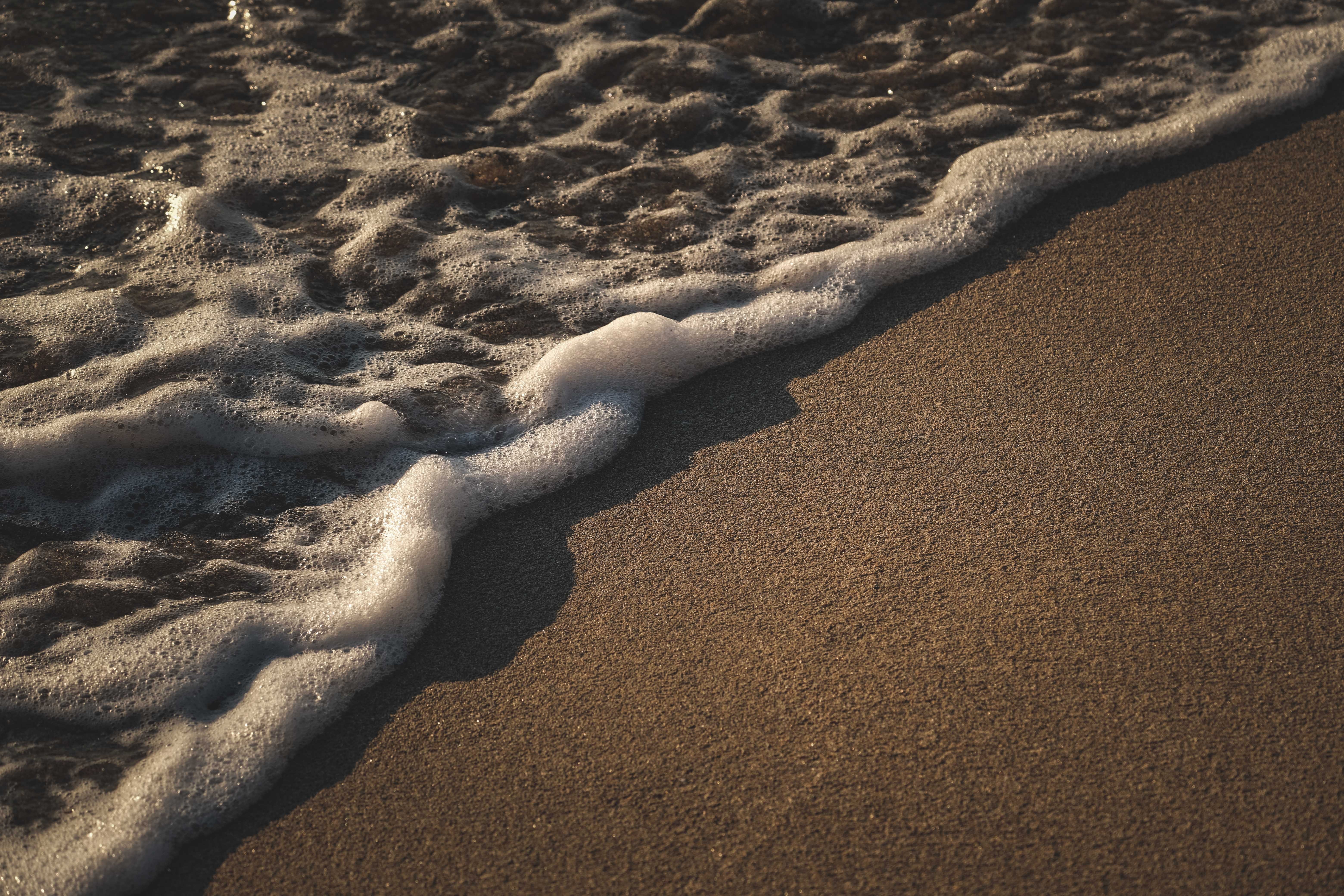 4K sea foam washing onto a sandy beach HD Wallpaper