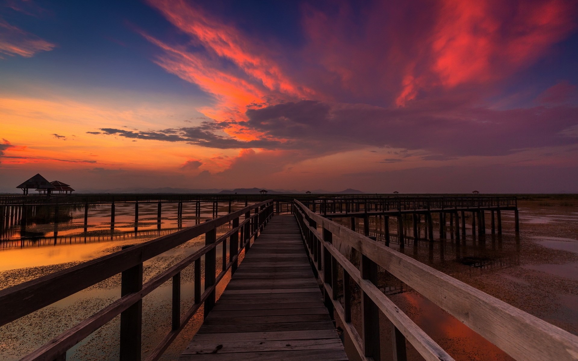 Wooden boardwalk over water at sunset with orange clouds HD Wallpaper