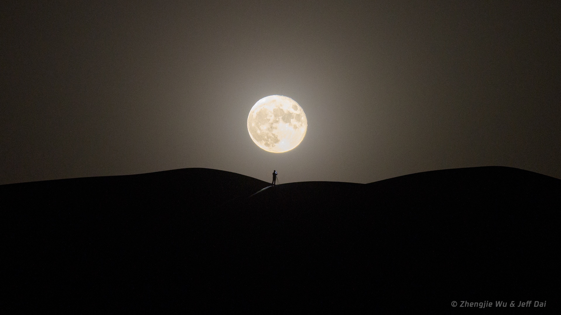 Silhouette of a person photographing the Moon over desert dunes HD Wallpaper
