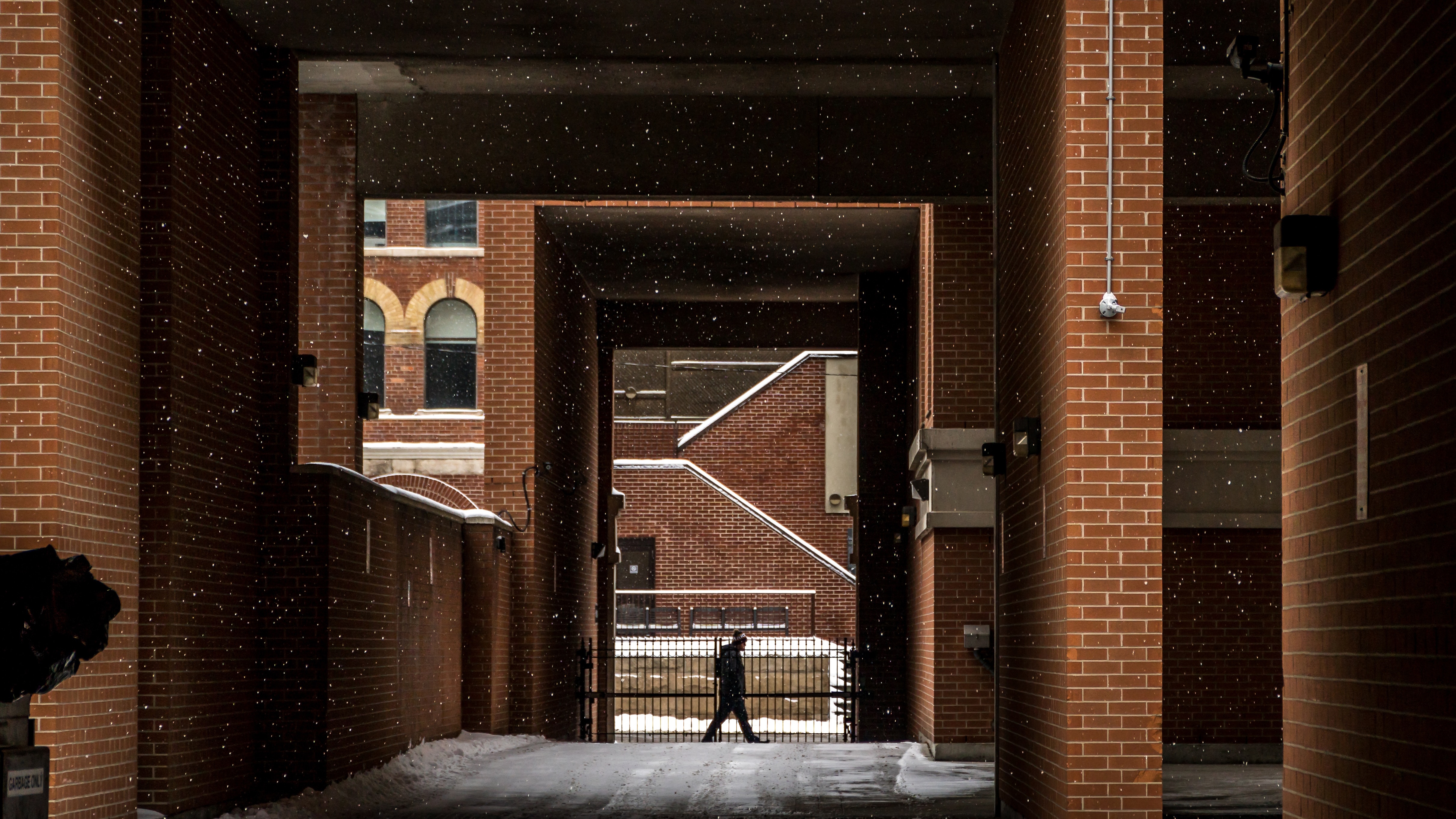Person walking in snow between brick buildings HD Wallpaper