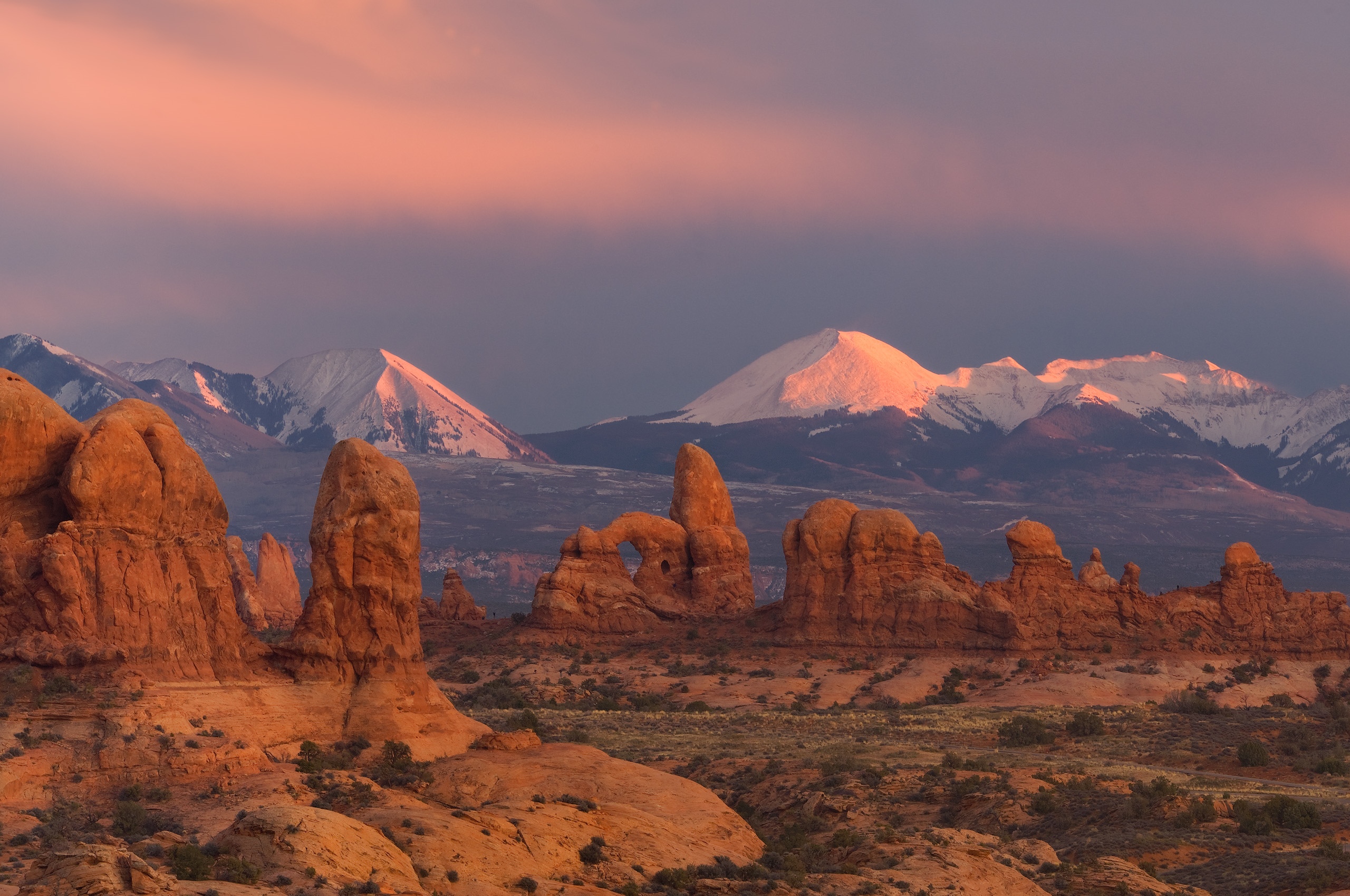 Desert rock formations with snow-capped mountains at sunrise HD Wallpaper