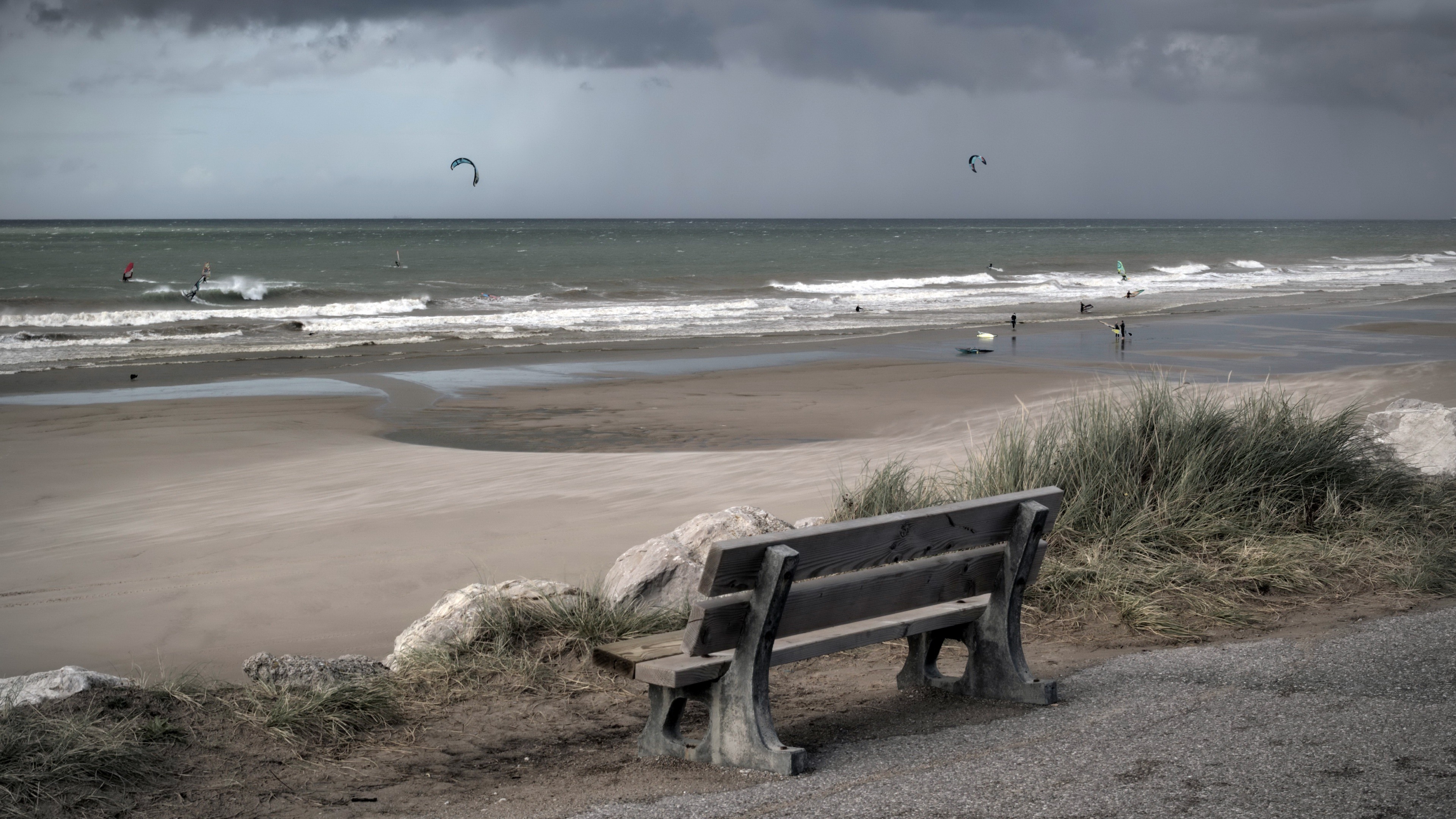 Beach with kite surfers and a bench HD Wallpaper
