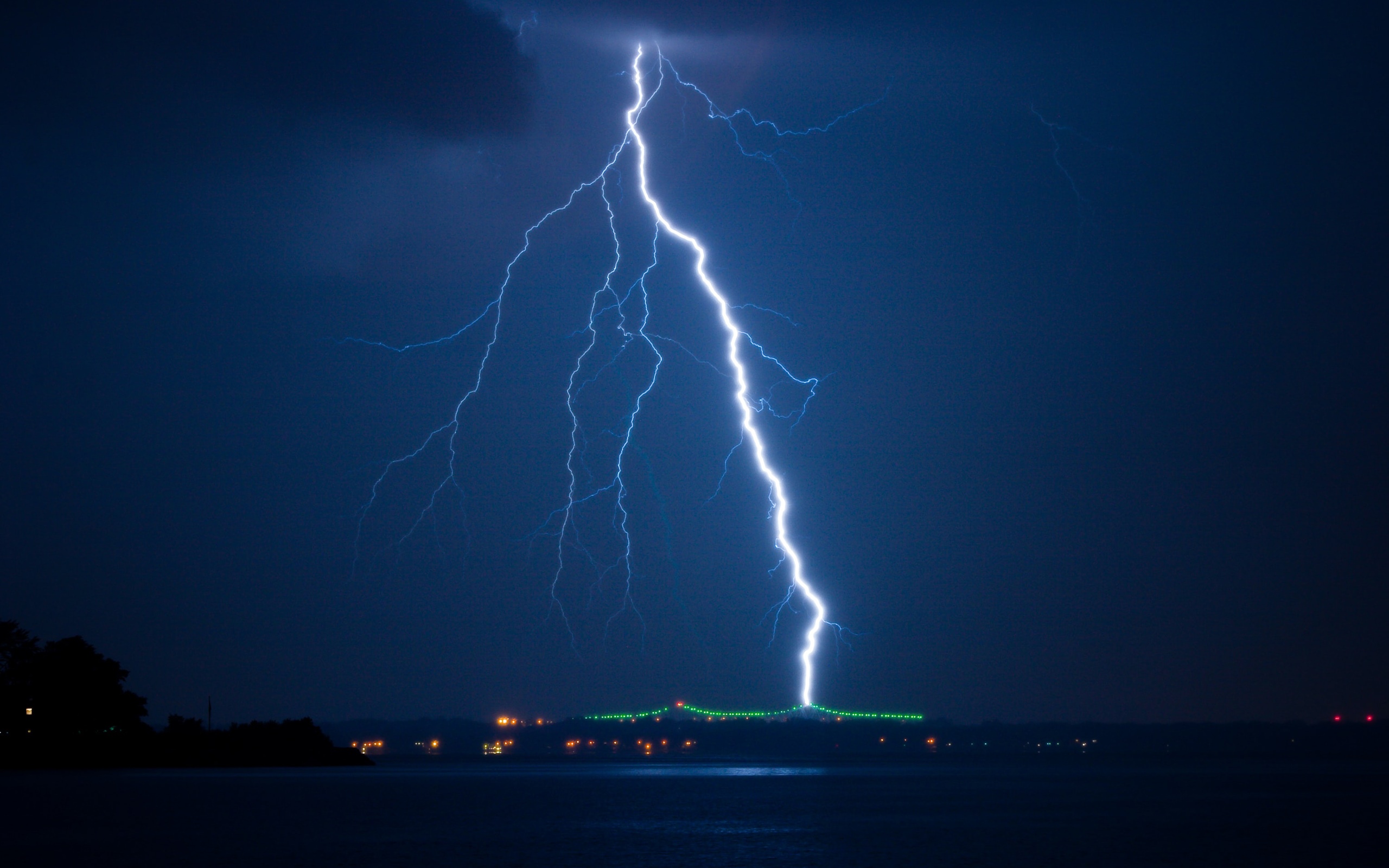 Lightning strikes over a body of water at night HD Wallpaper