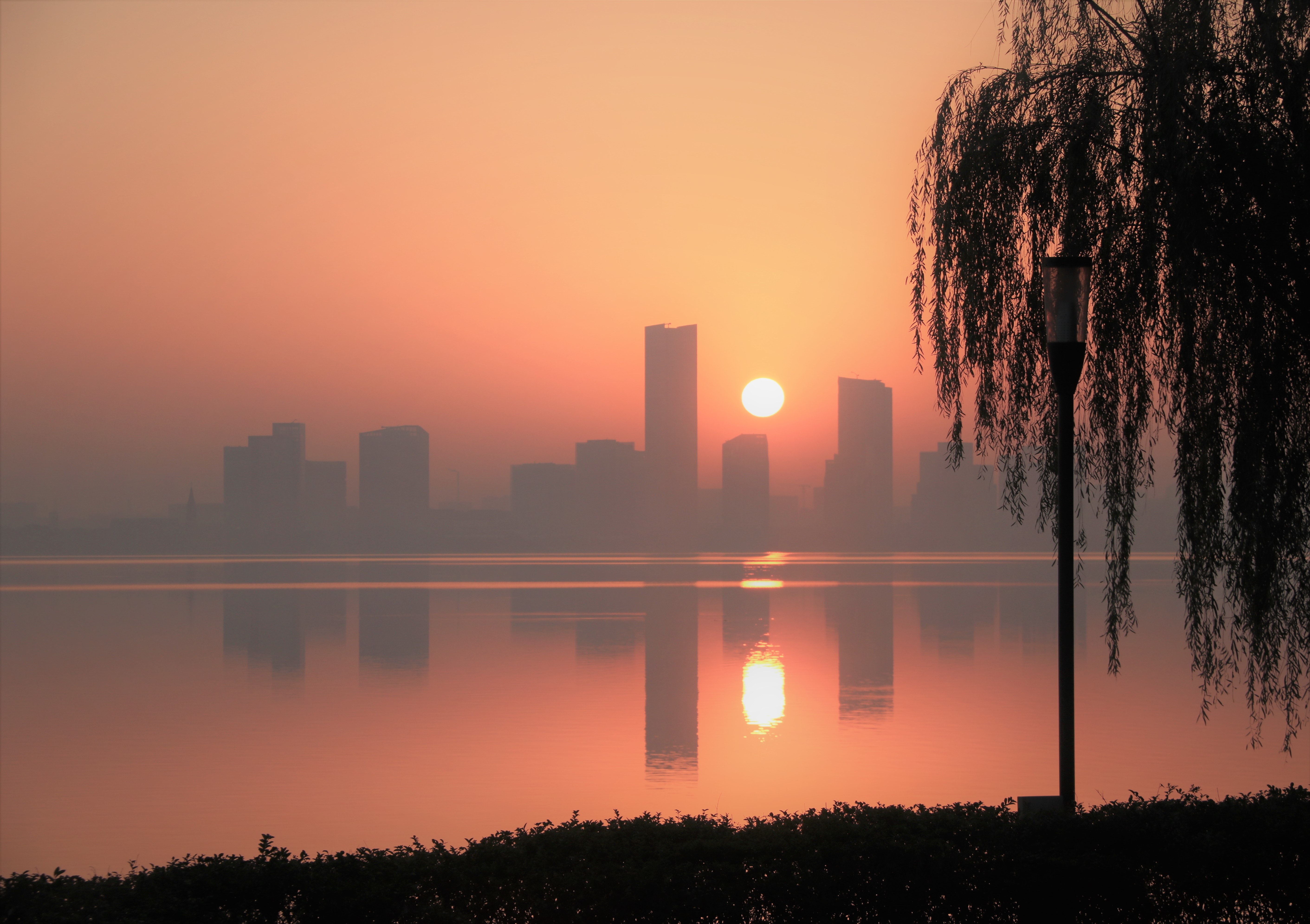 Sunrise over a misty city skyline reflected in a lake HD Wallpaper