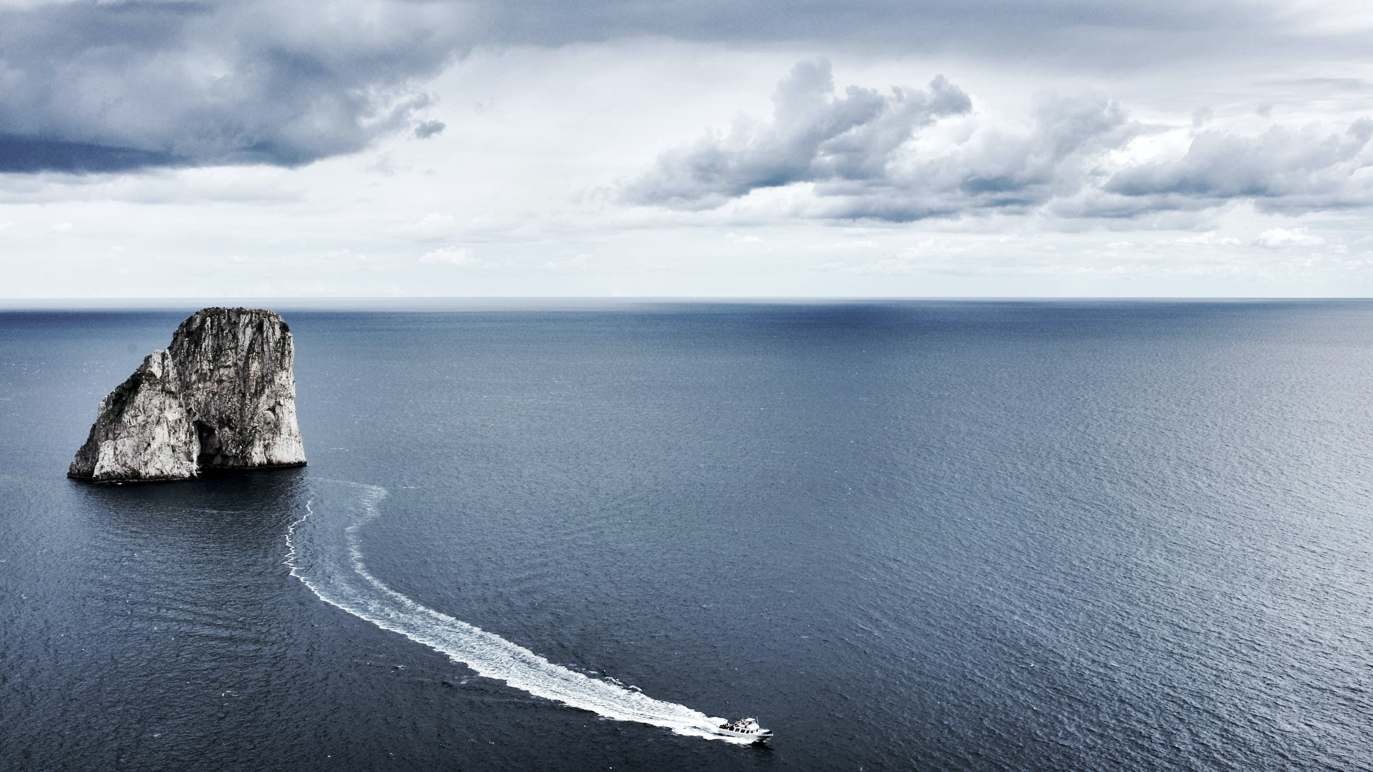 4K sea rock formation with boat and clouds HD Wallpaper