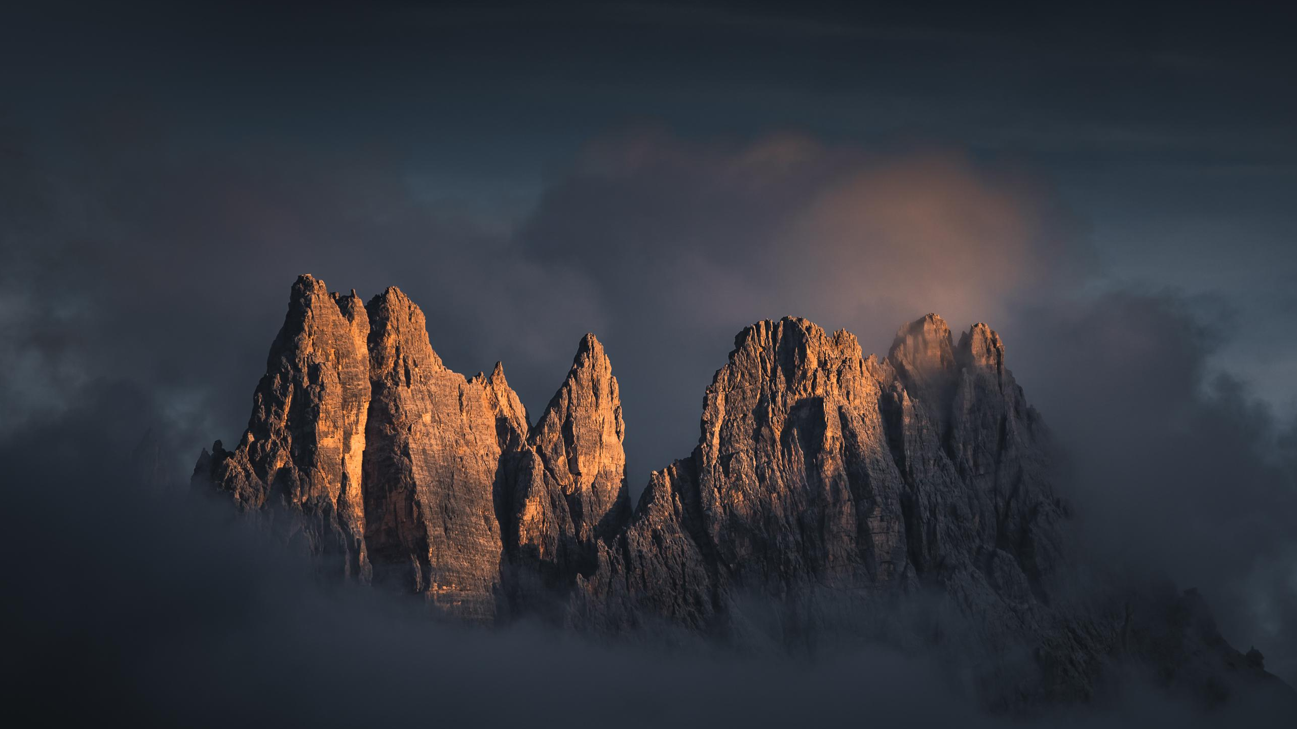 Jagged mountain peaks emerge from clouds at sunset HD Wallpaper