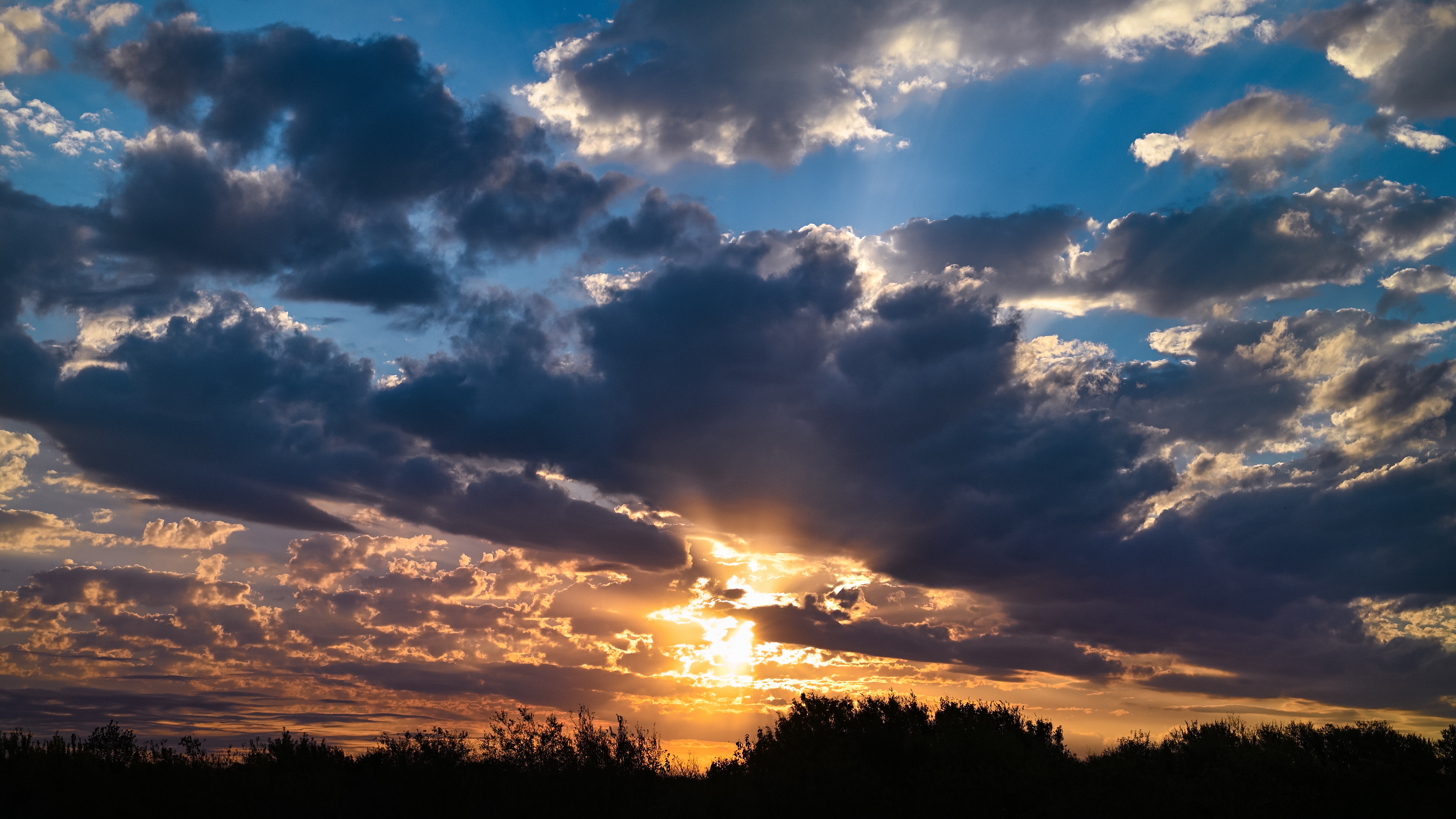 4K Sunset with Dramatic Clouds Over Silhouetted Trees HD Wallpaper