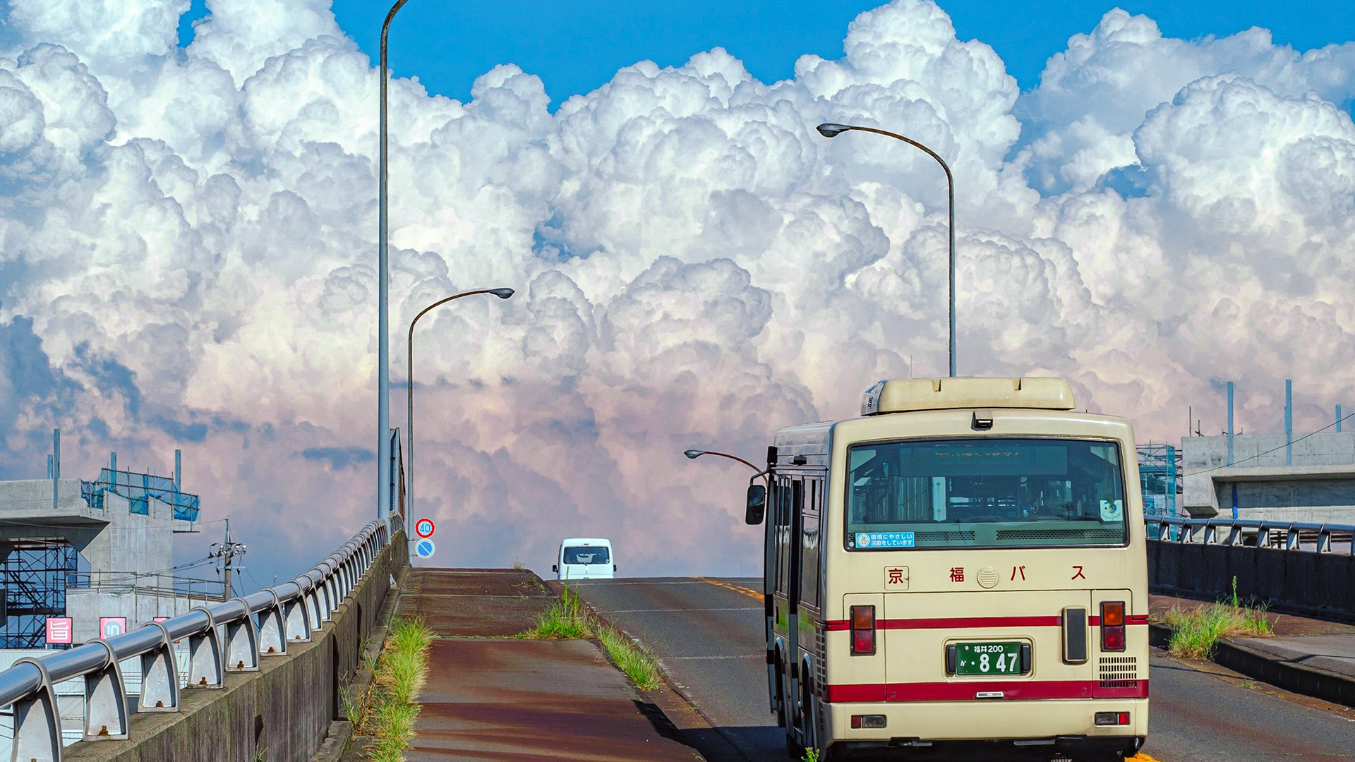 A bus drives up a road under a cloudy sky HD Wallpaper