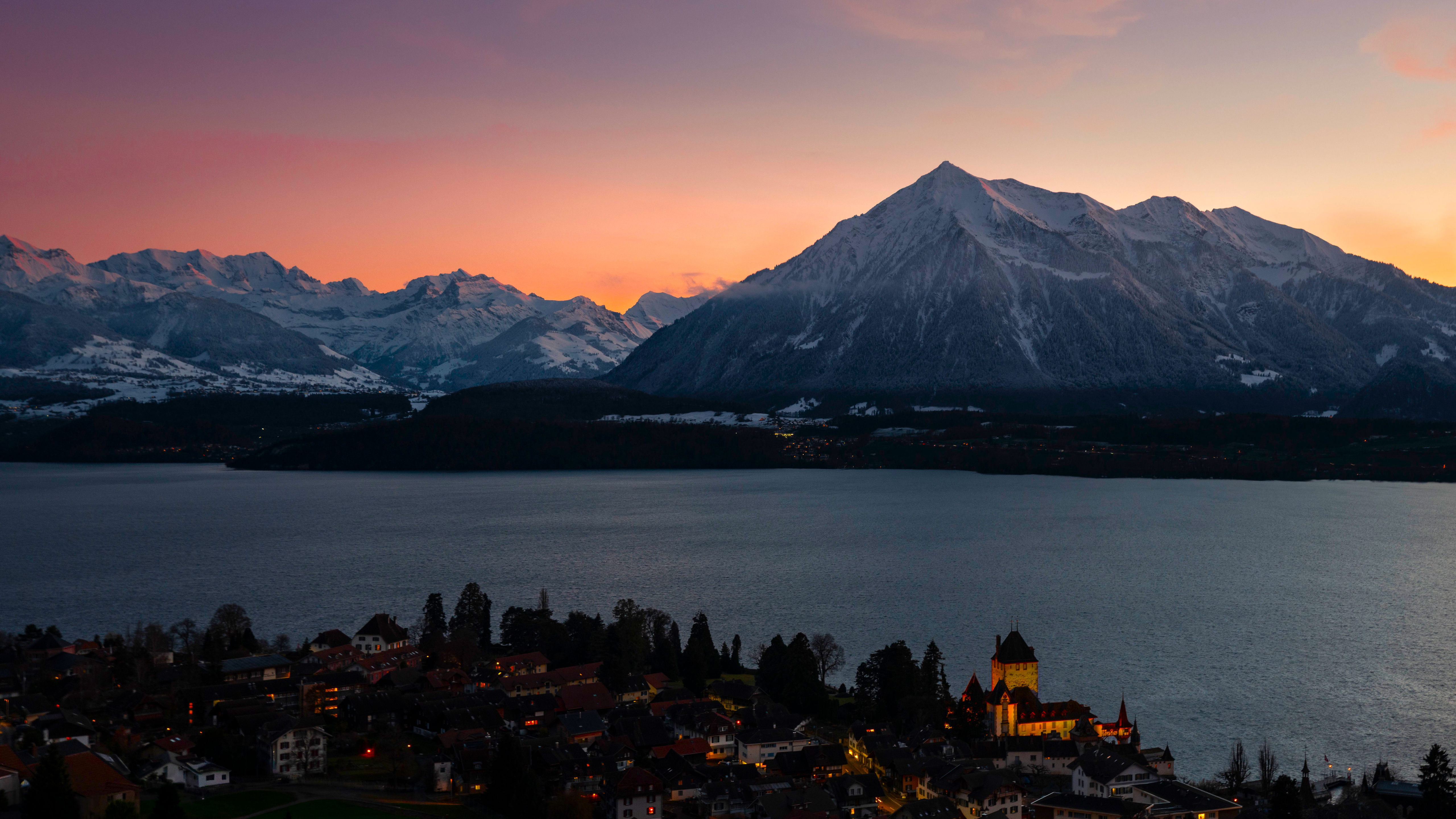 Sunset over a lake with snow-capped mountains and a village HD Wallpaper