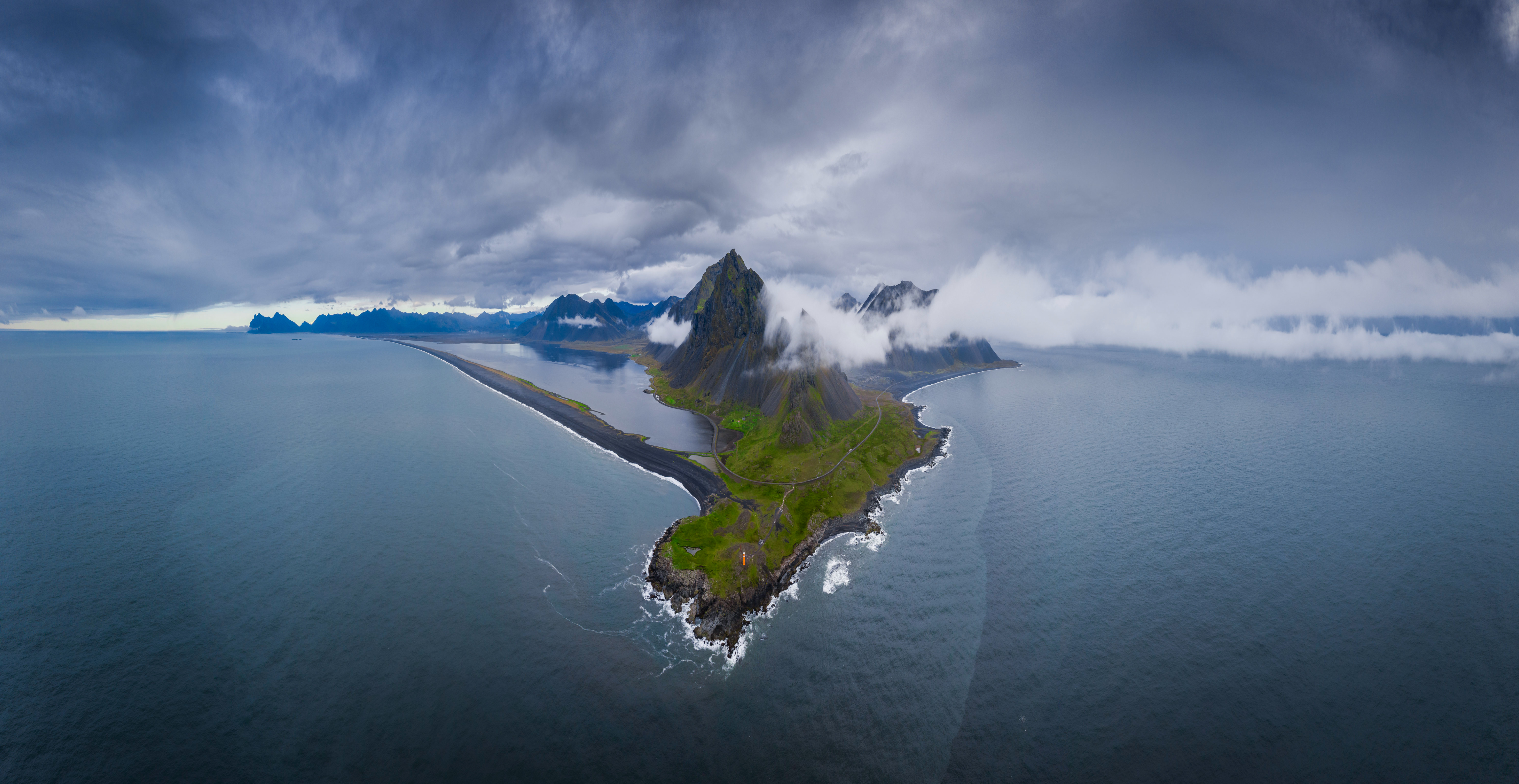Aerial view of a green island with a black sand beach HD Wallpaper