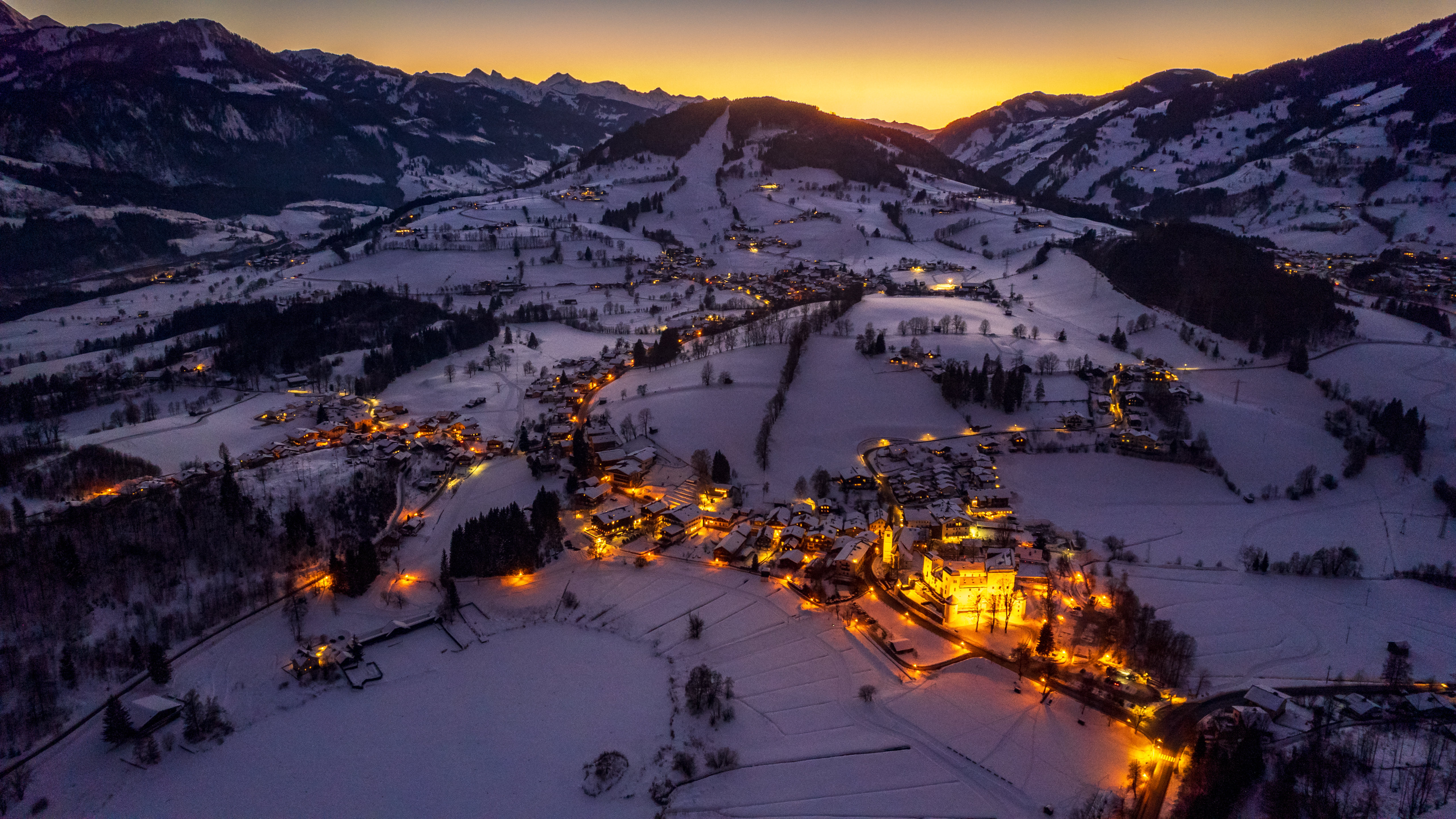 Snowy village nestled in mountains at sunset HD Wallpaper