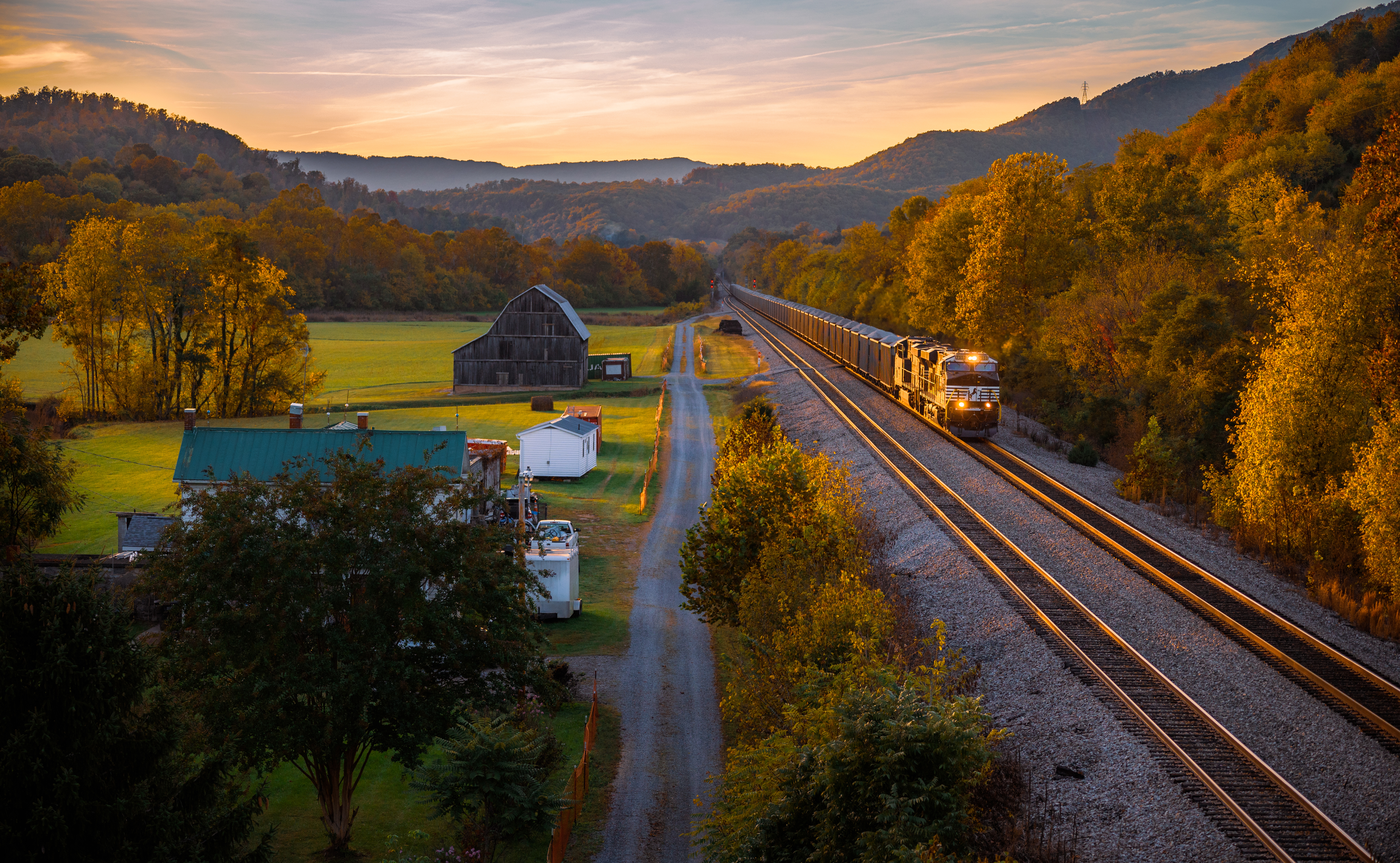 Train with headlights in a rural landscape at sunset HD Wallpaper