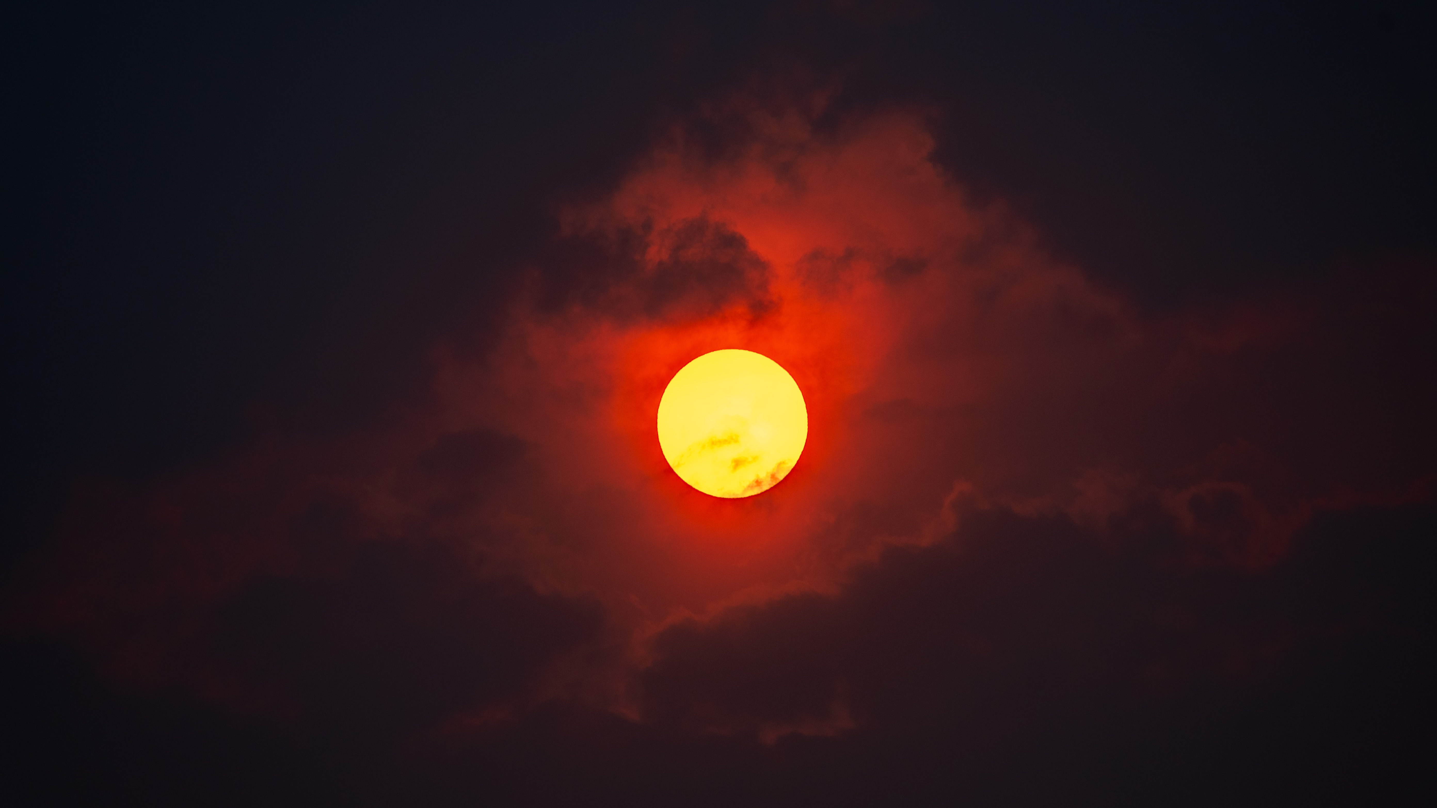 Red sun obscured by dark clouds at dusk HD Wallpaper