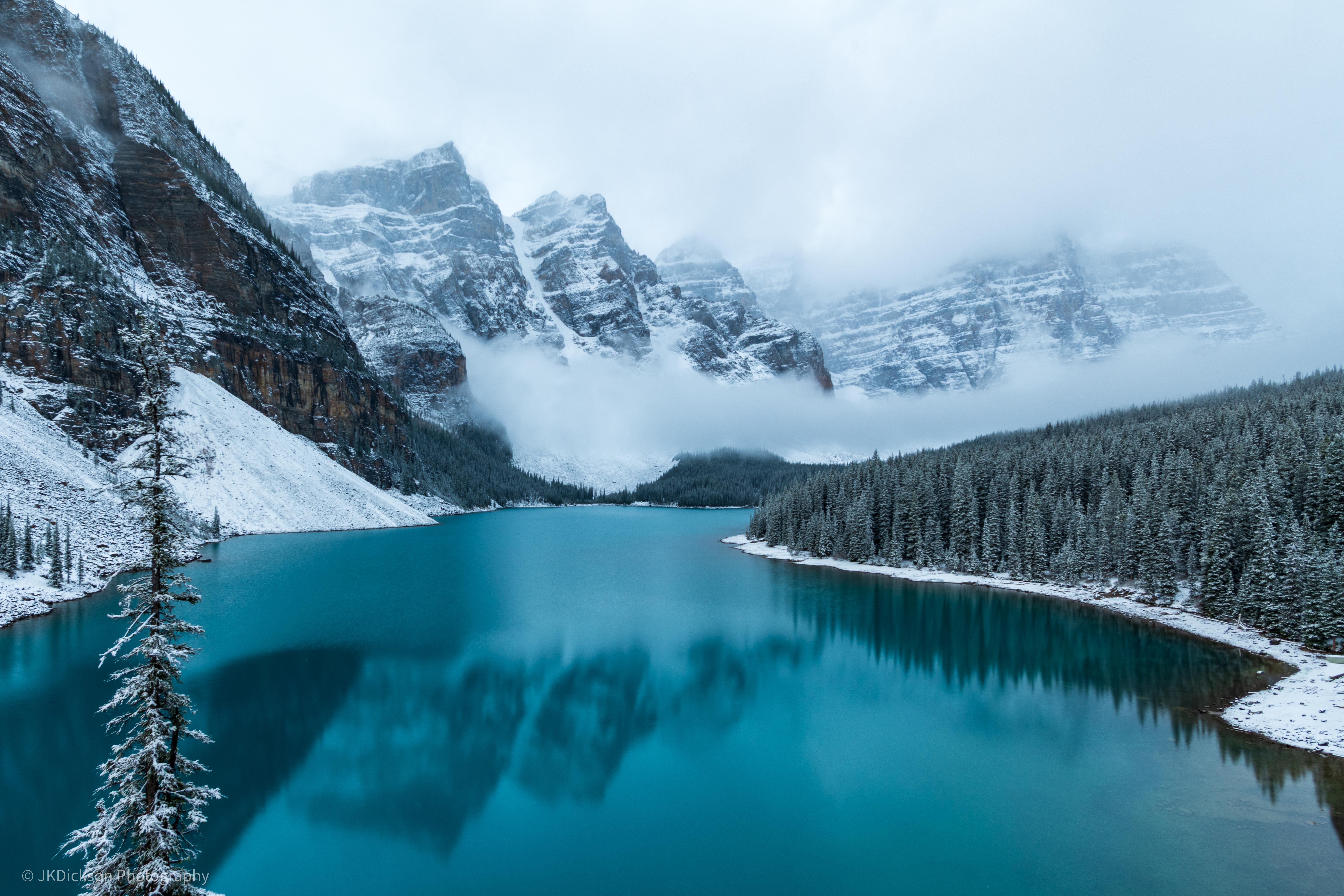 Snowy mountains and pine forest reflected in a turquoise lake HD Wallpaper