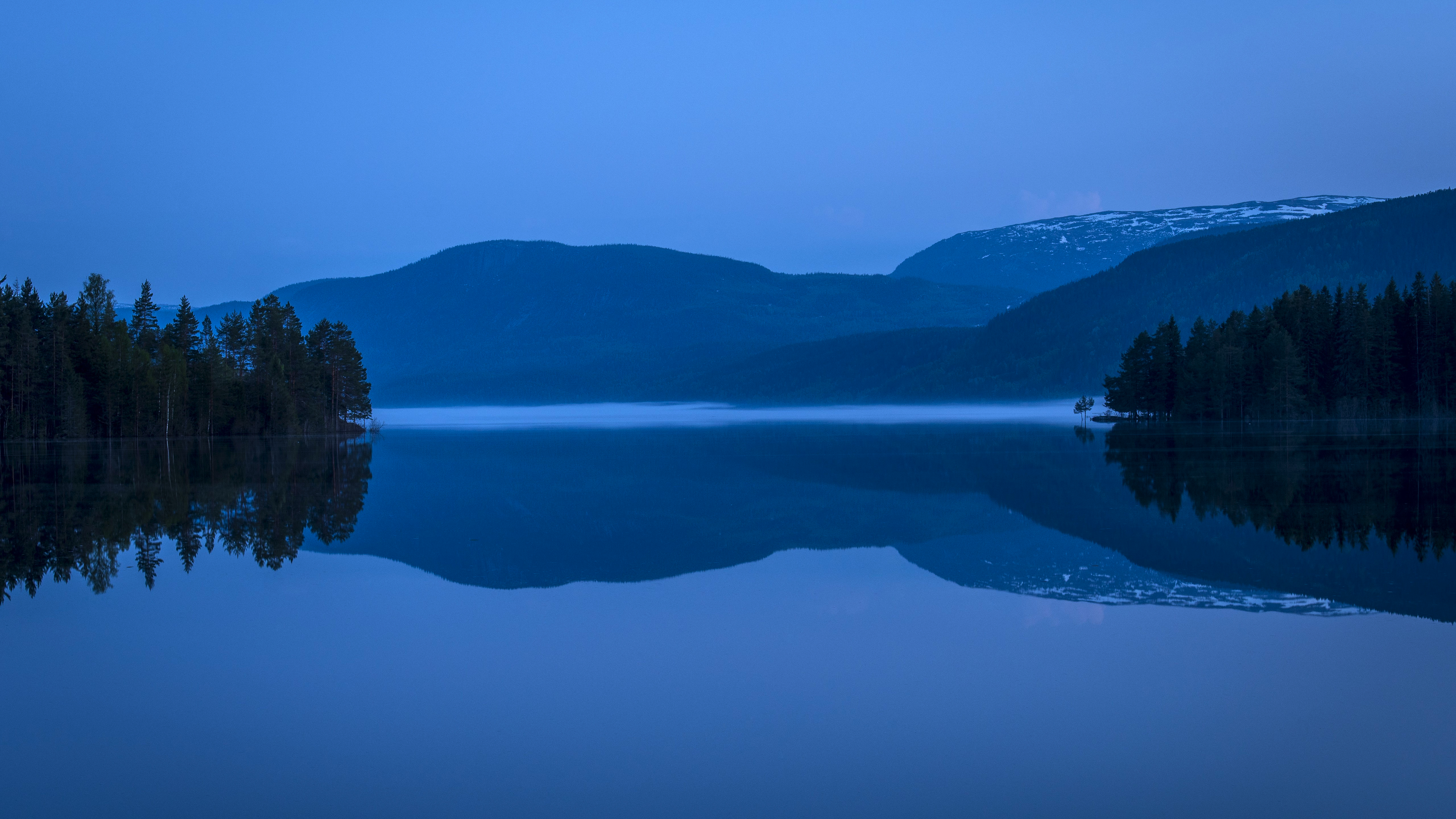 Misty mountains reflected in a dark lake at twilight HD Wallpaper