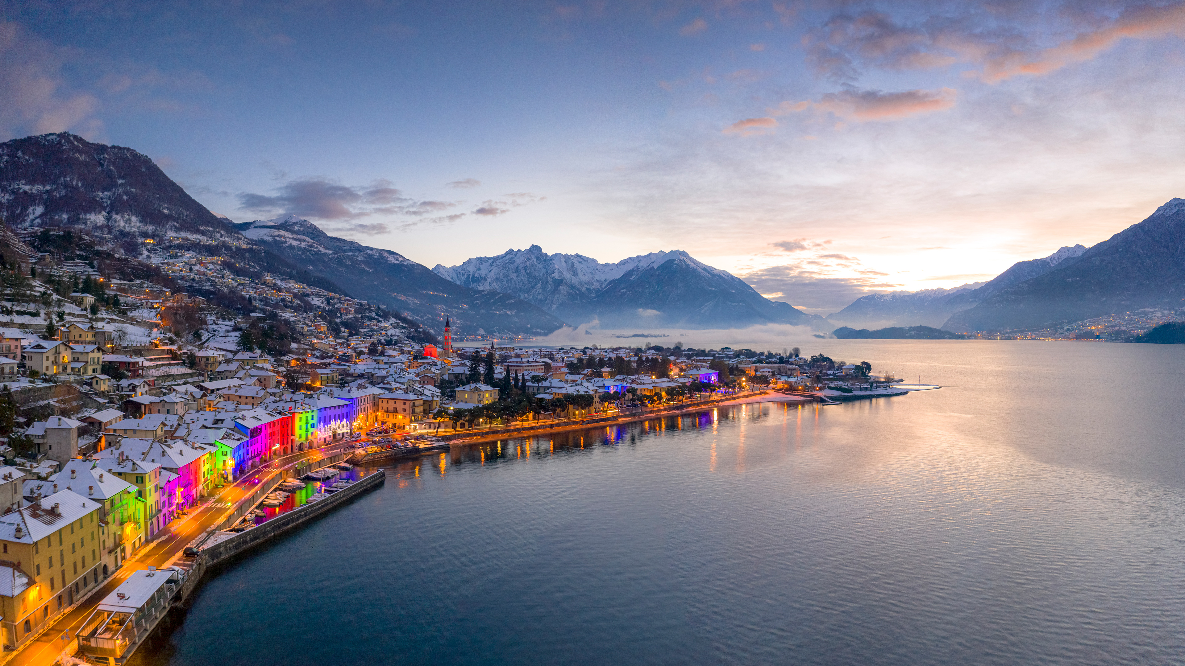 Colorful town lights along a snowy waterfront at dusk HD Wallpaper