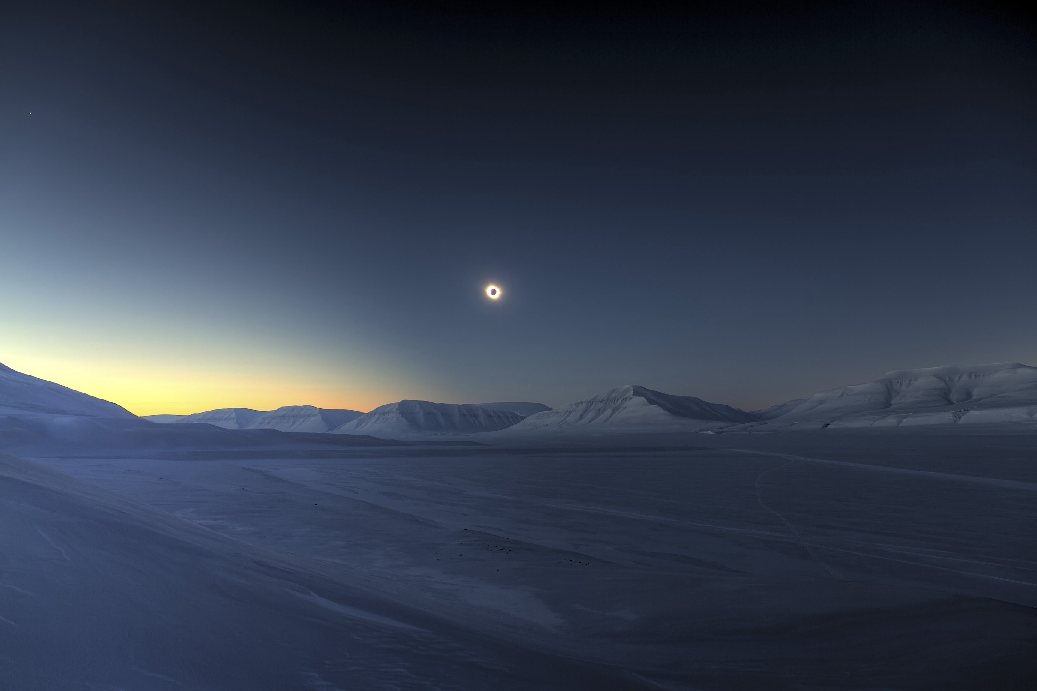 Solar eclipse over snow-covered mountains at twilight HD Wallpaper