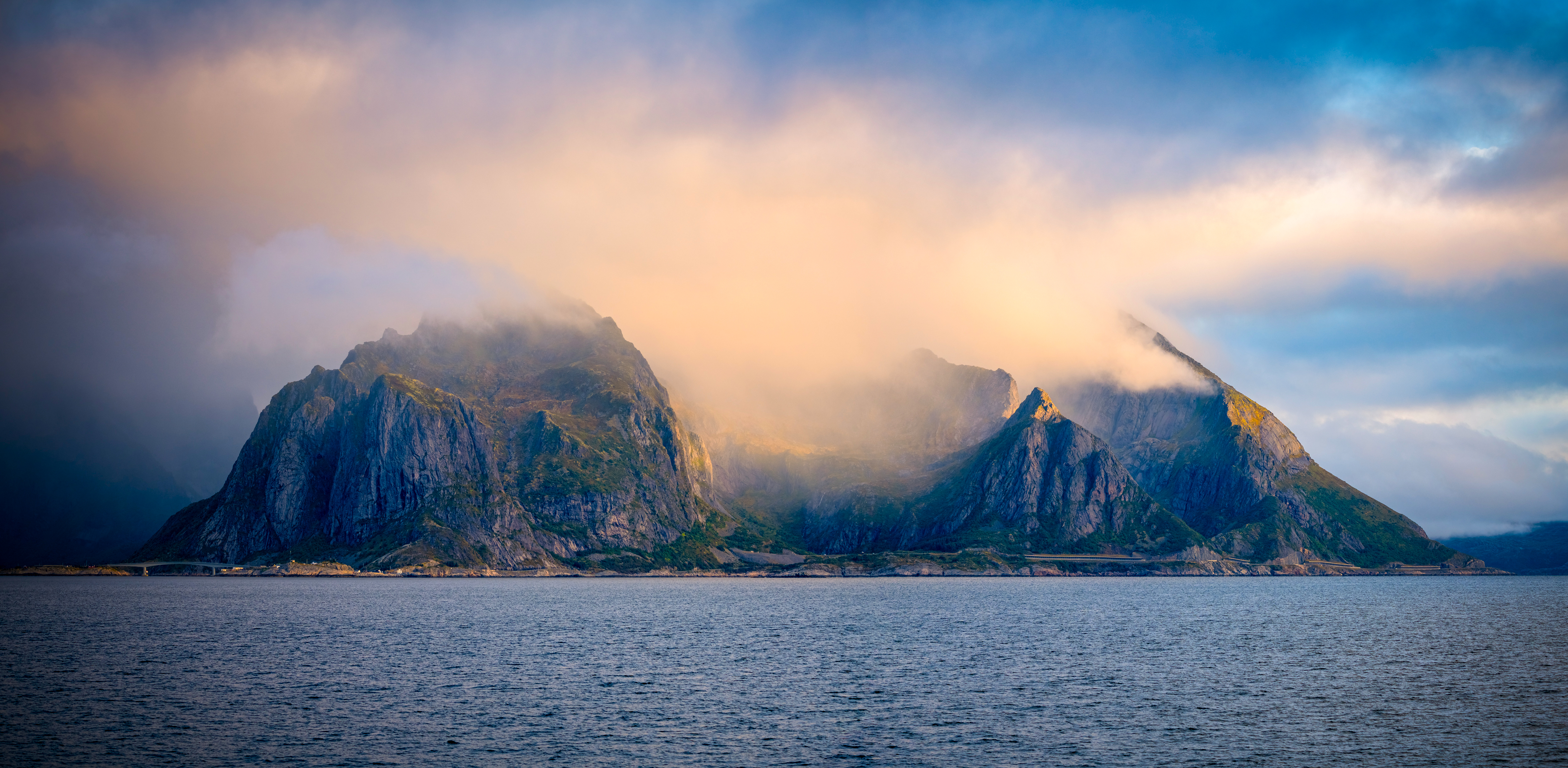 Misty mountains rise from the sea under cloudy sky HD Wallpaper
