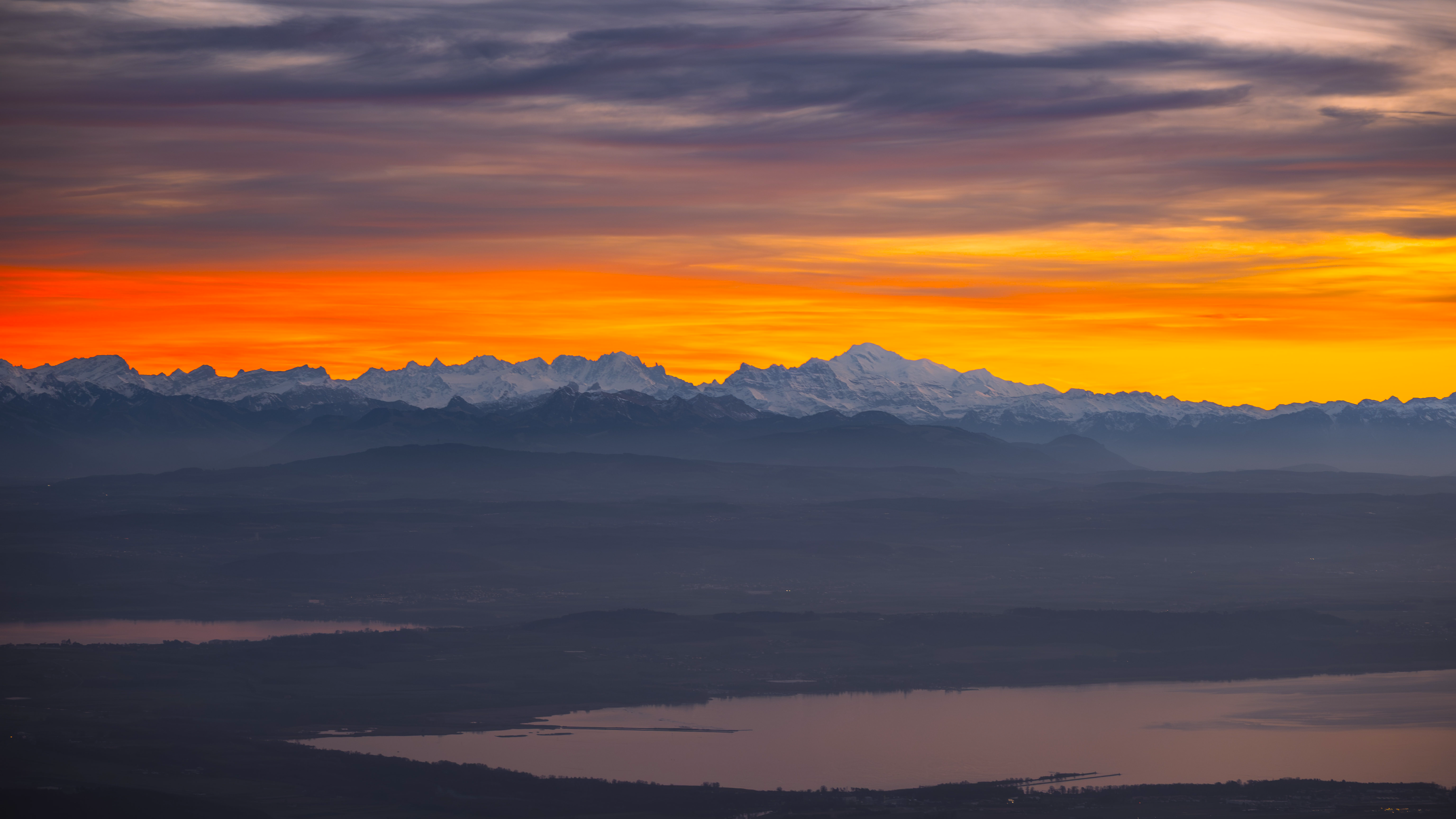 Aerial view of snowy mountain peaks over a lake at sunset HD Wallpaper