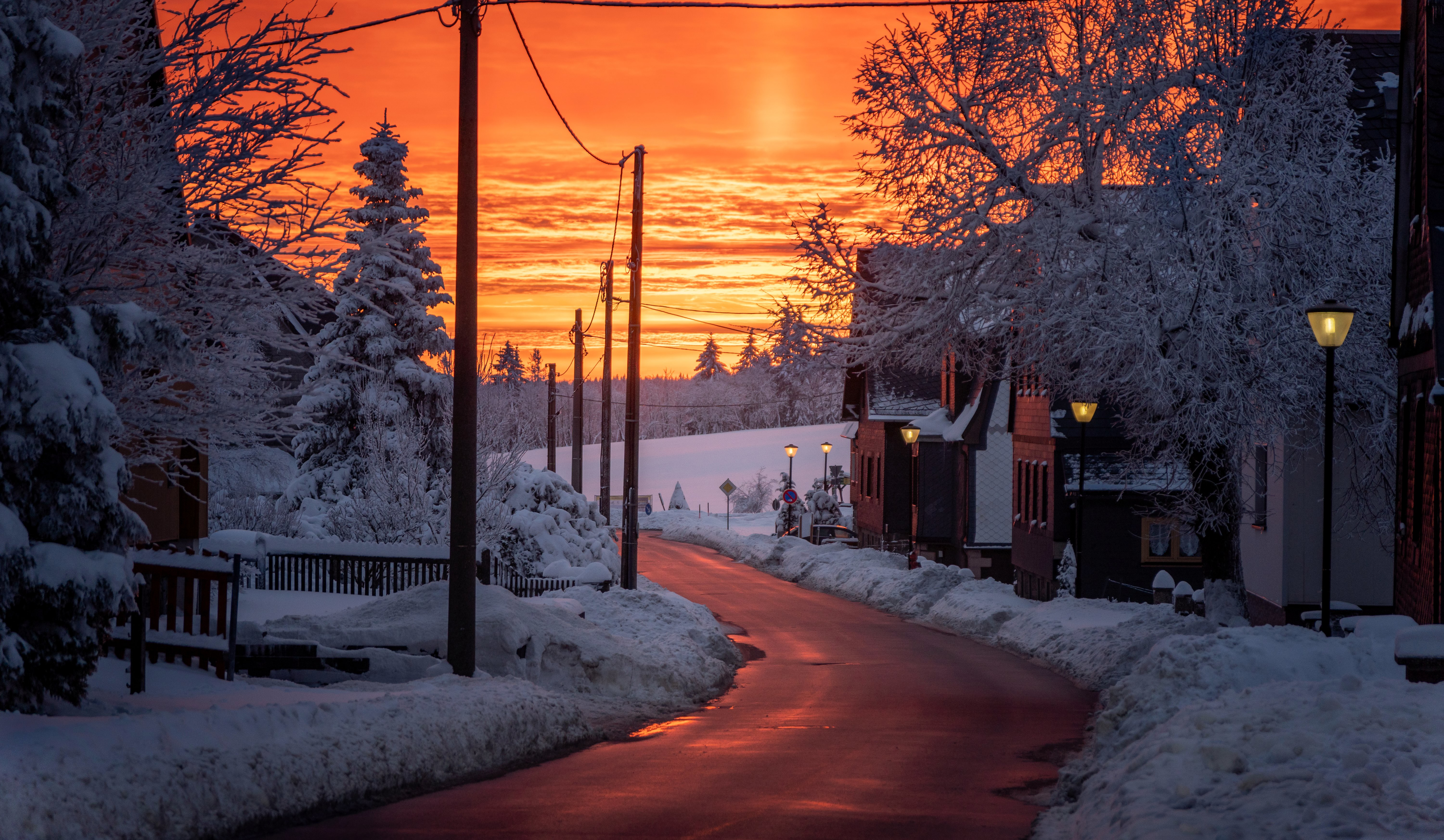 Snowy road at sunset with orange sky and power lines HD Wallpaper