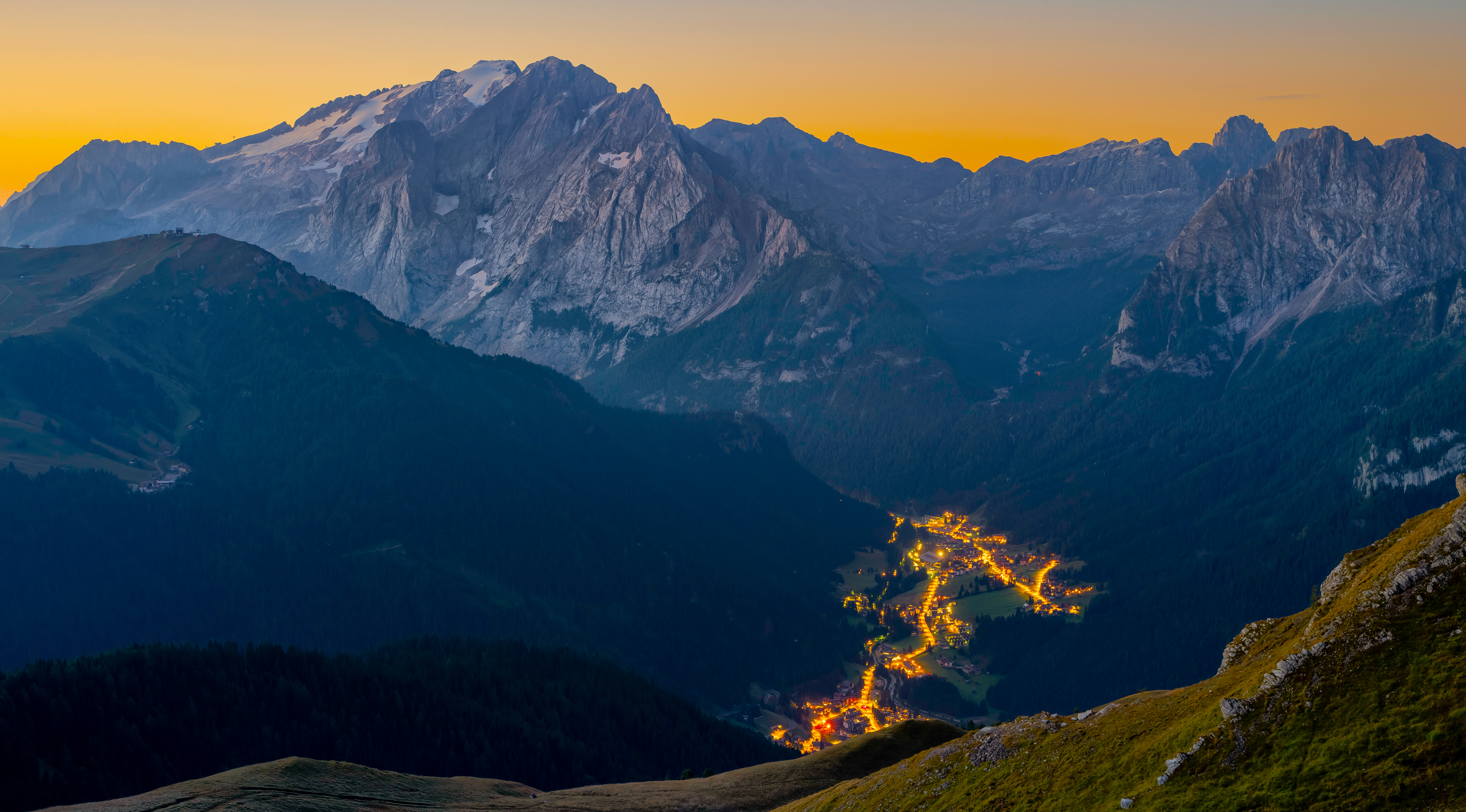 Village lights glow in a mountain valley at dusk HD Wallpaper