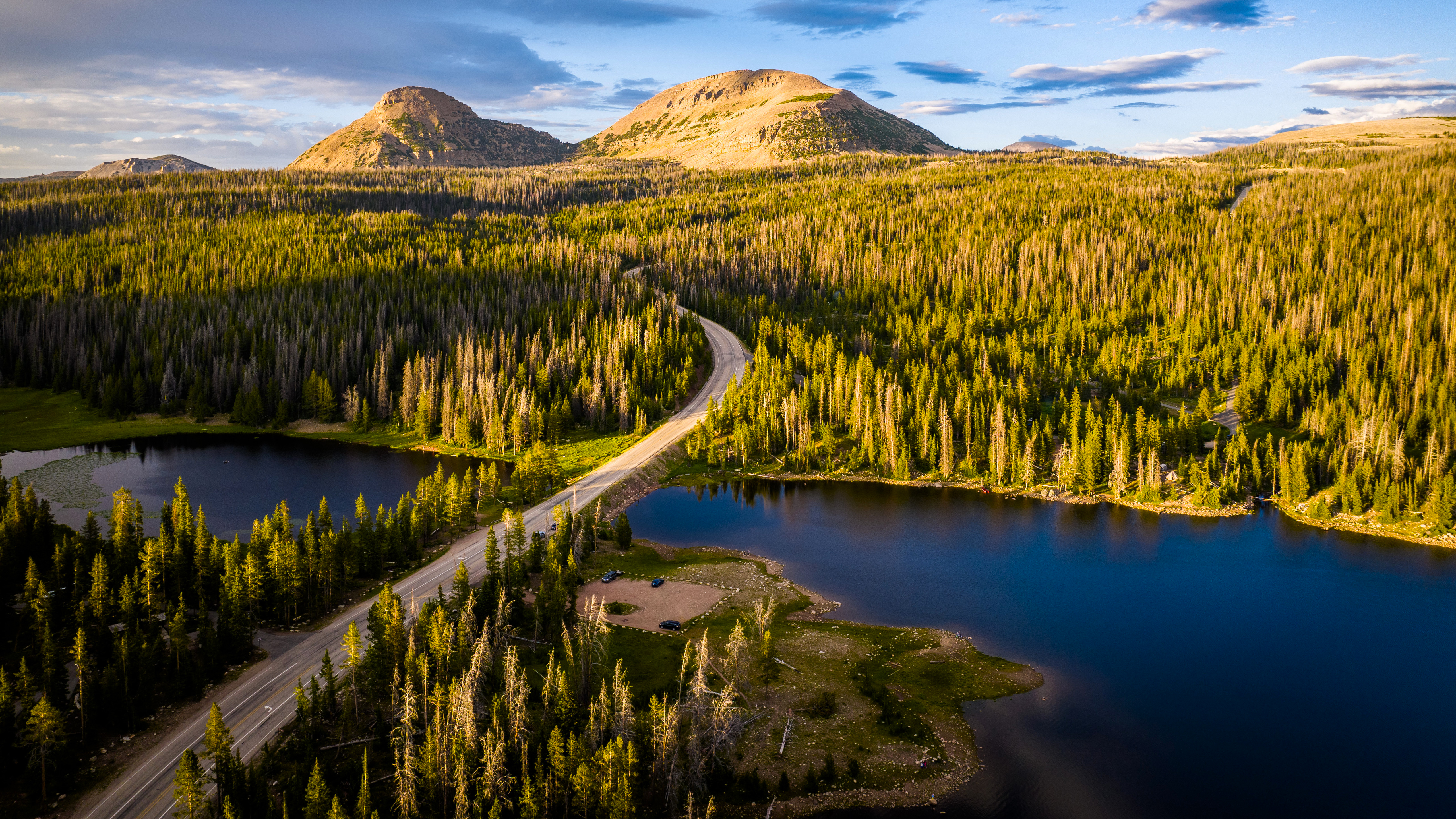 Aerial view of a road through a forest with mountains HD Wallpaper