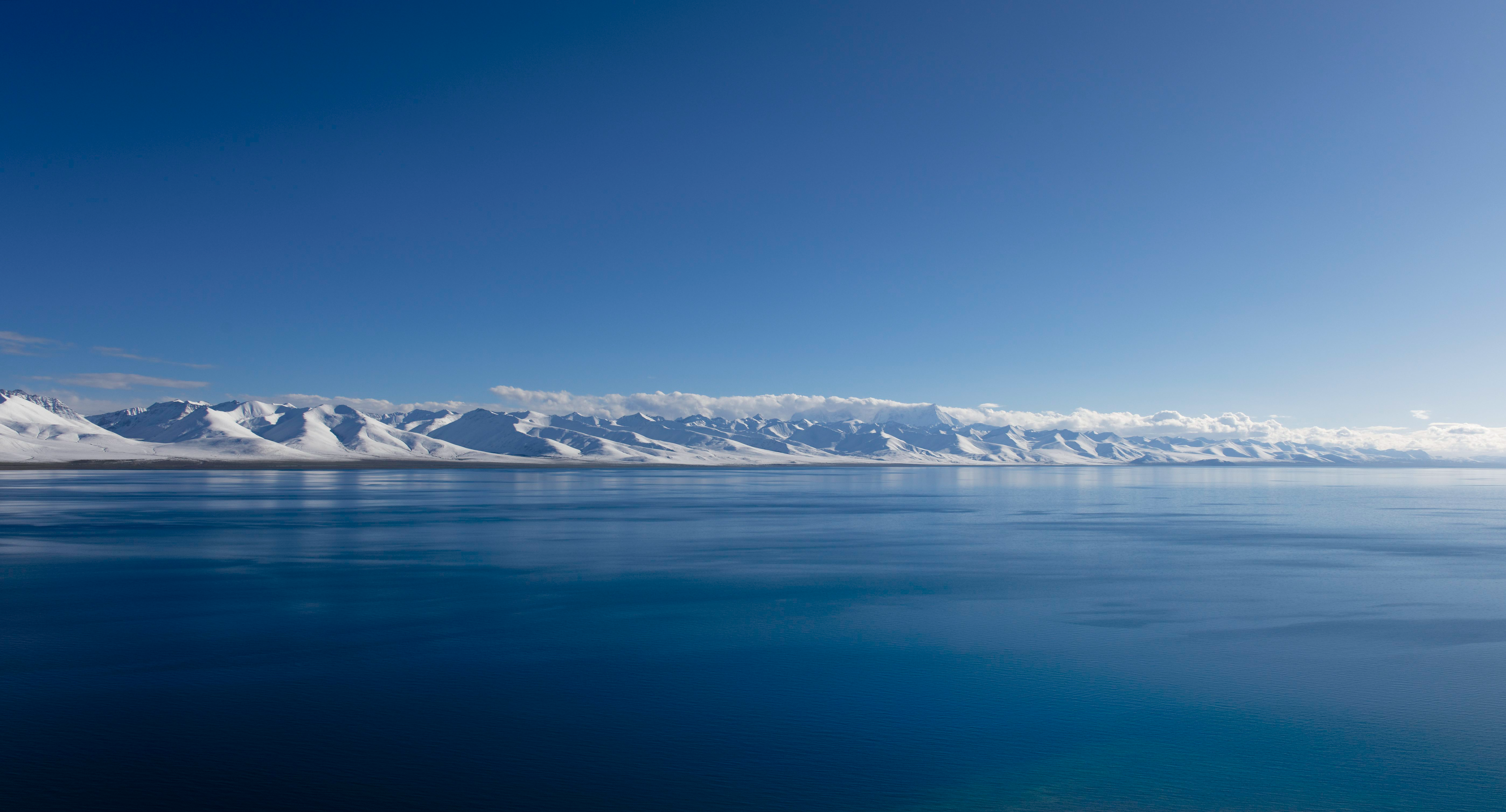 Snow-covered mountains across a vast blue lake HD Wallpaper
