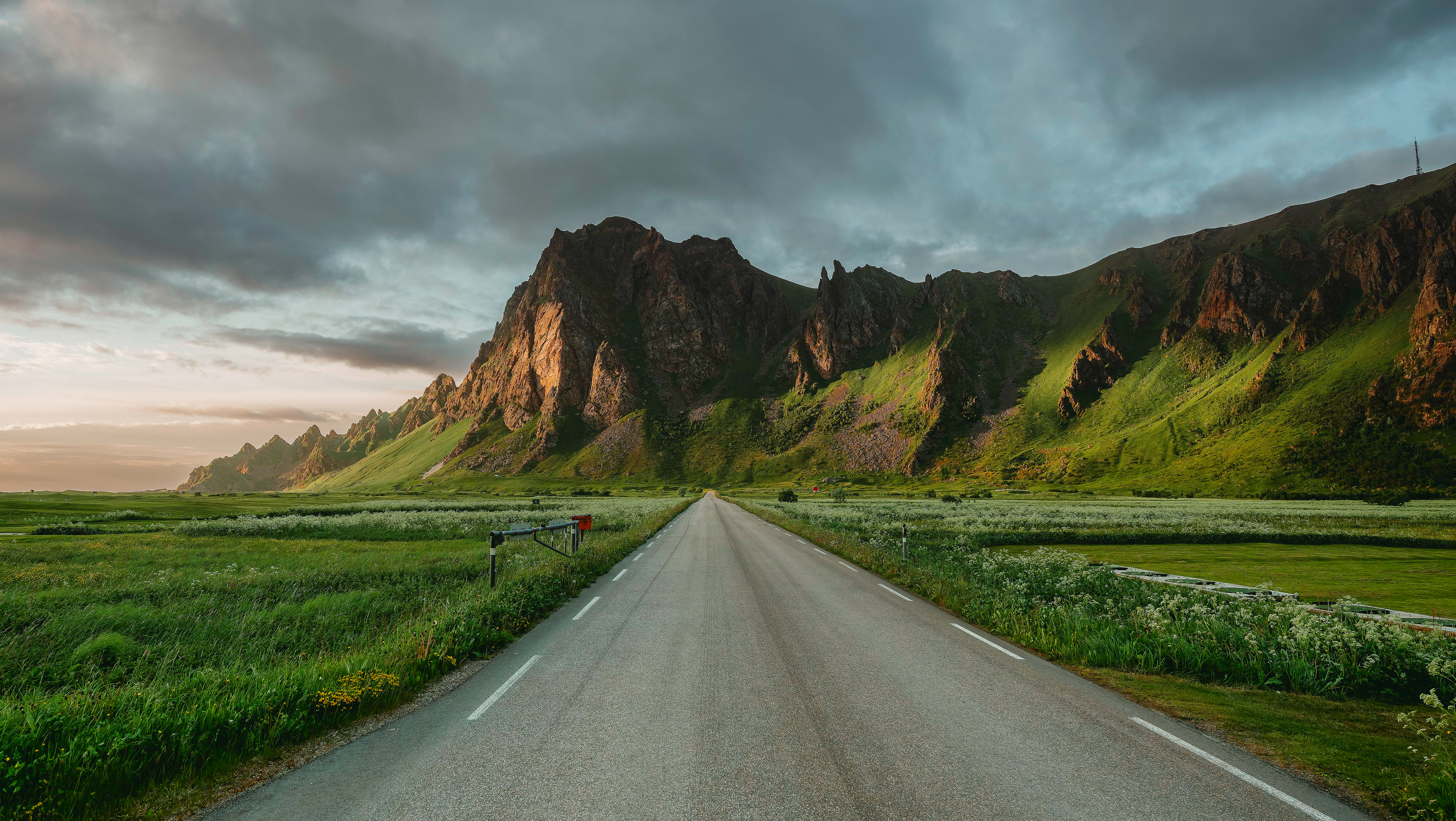 Road leading to mountains under cloudy sky HD Wallpaper