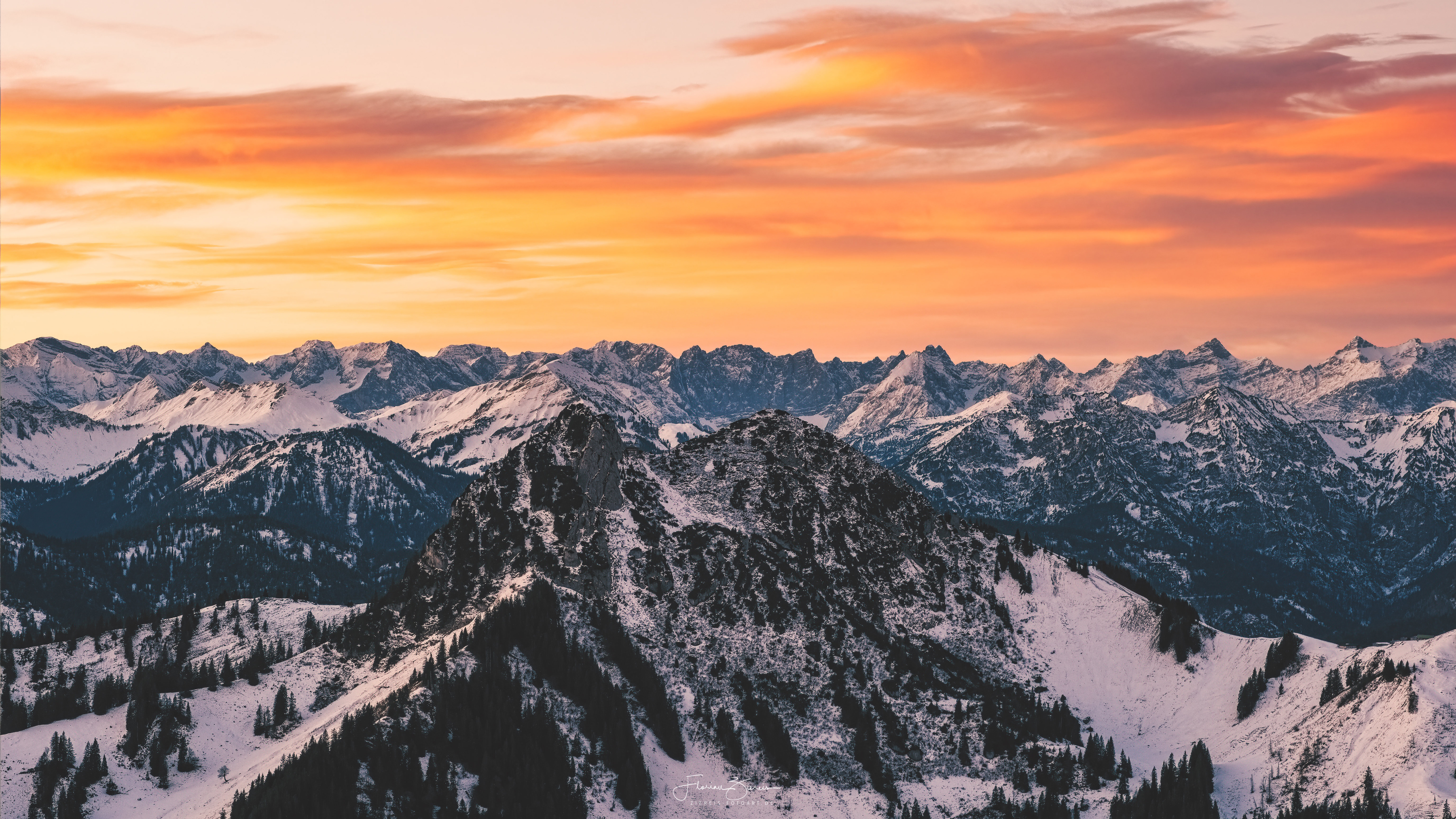 Snow-covered mountains under orange sunset sky HD Wallpaper