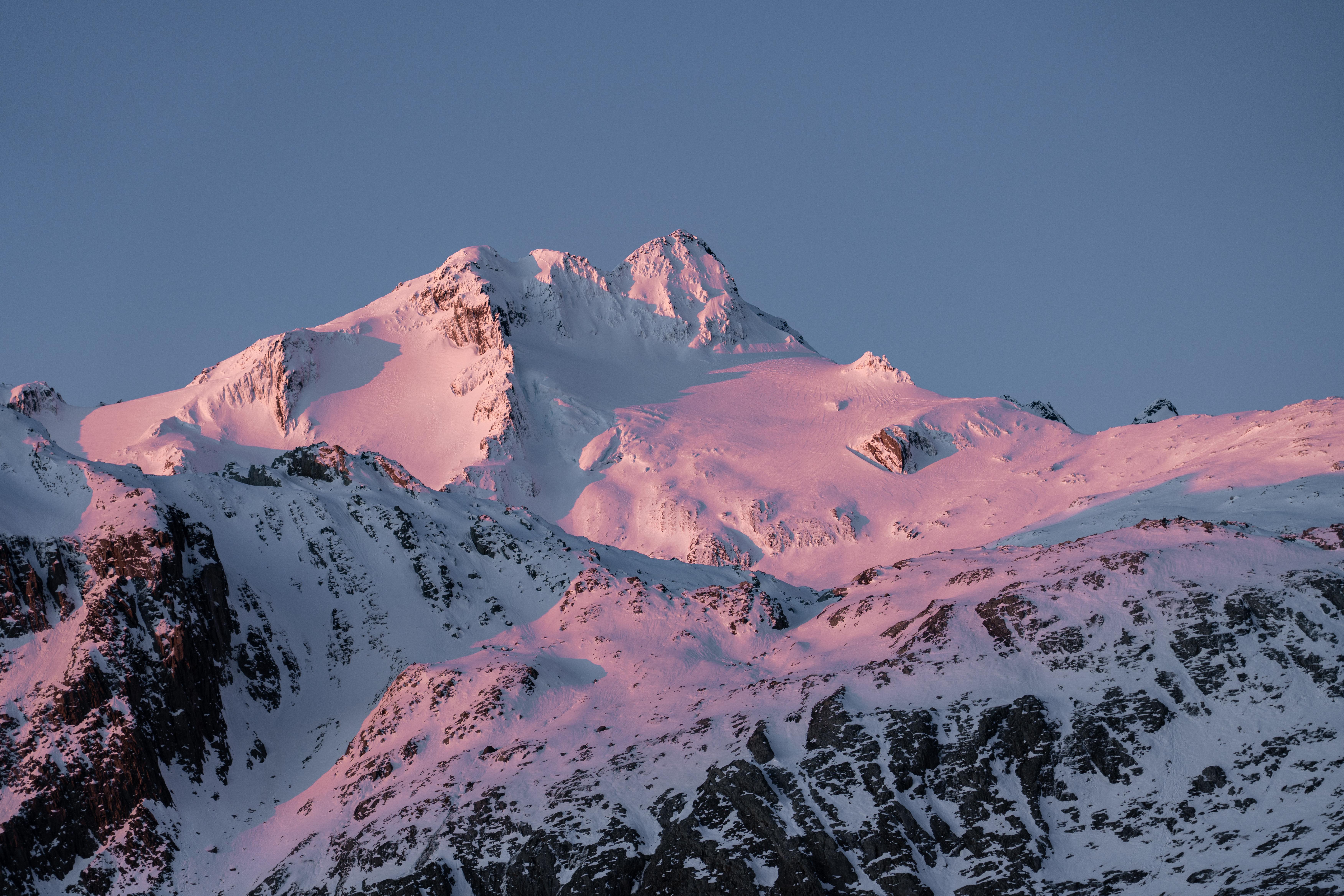 Snow-covered mountains bathed in pink sunset light HD Wallpaper