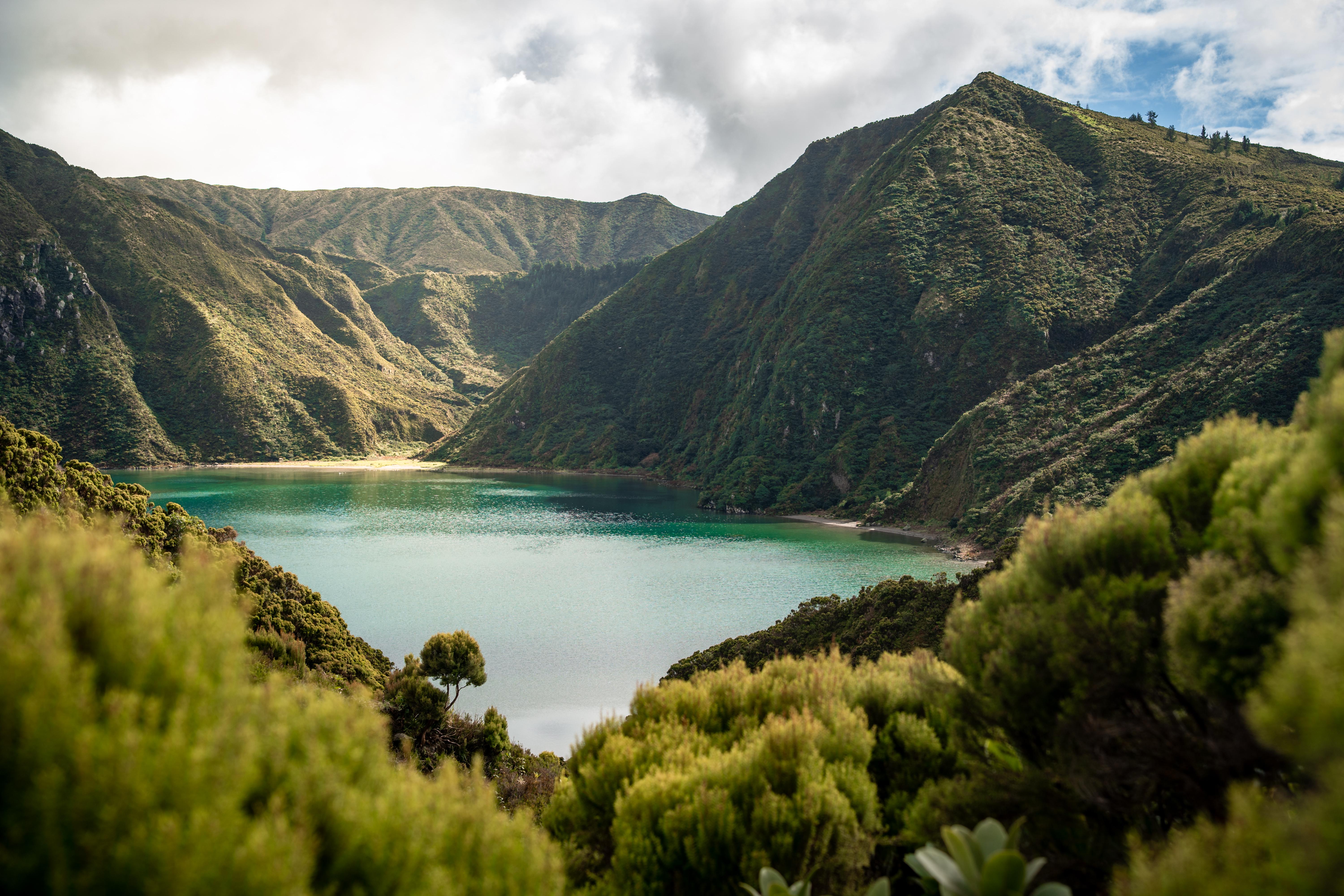 Volcanic lake surrounded by green hills under clouds HD Wallpaper