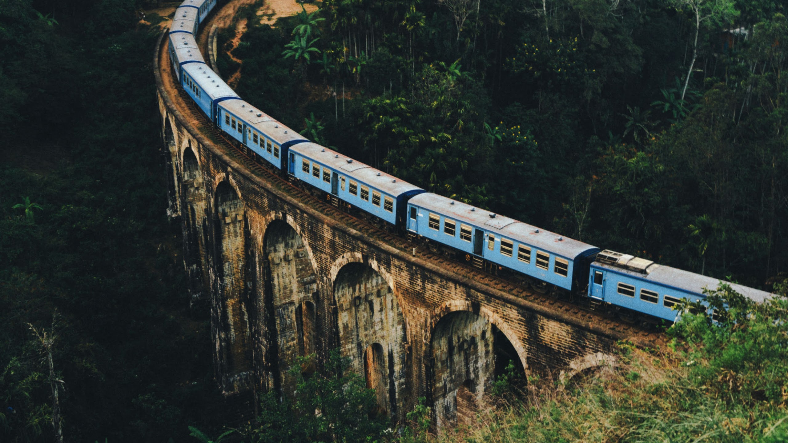 Blue train crossing a historic nine-arch railway bridge in Sri Lanka HD Wallpaper