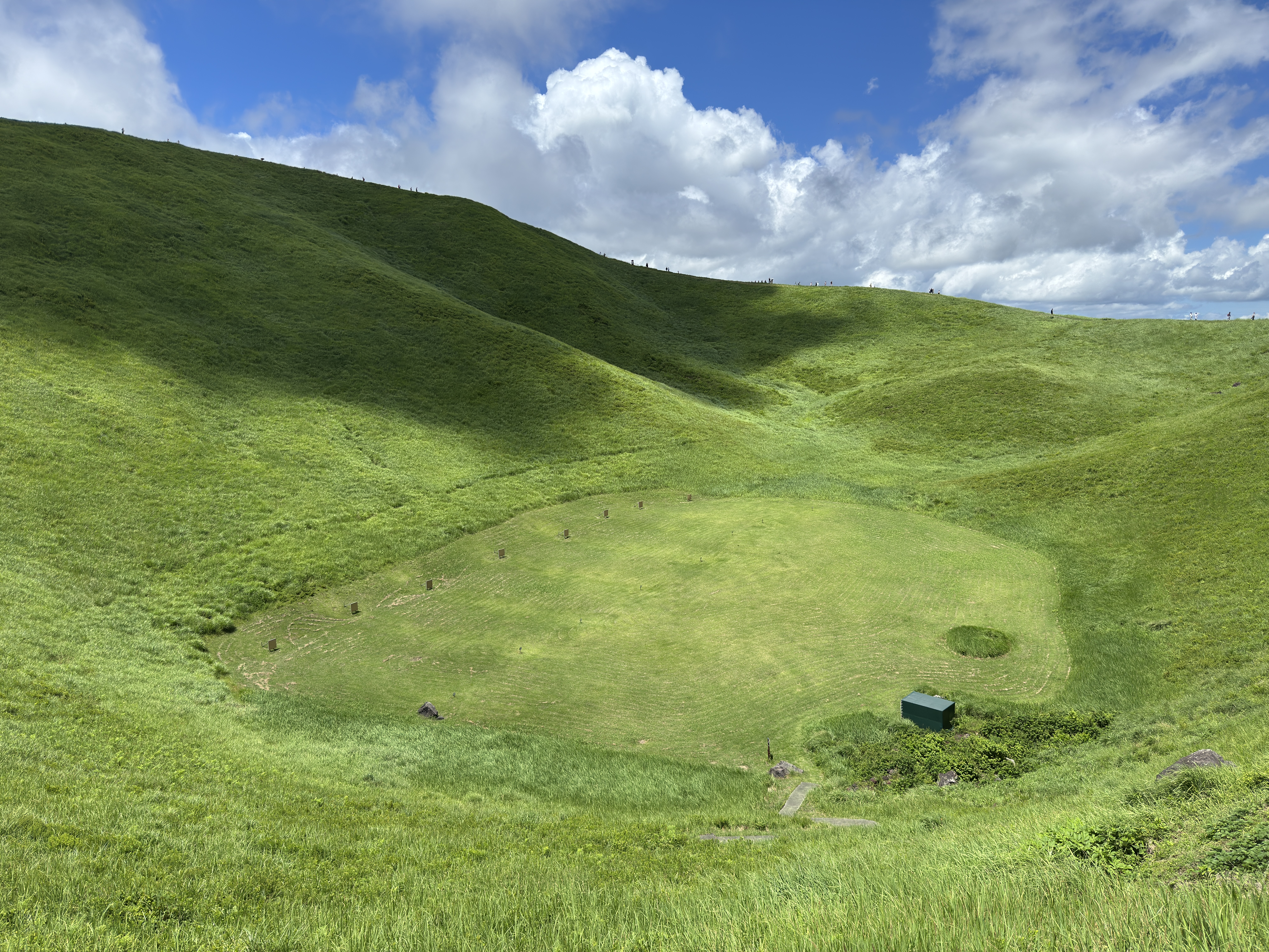 Green grassy crater with a small shelter under a cloudy sky HD Wallpaper