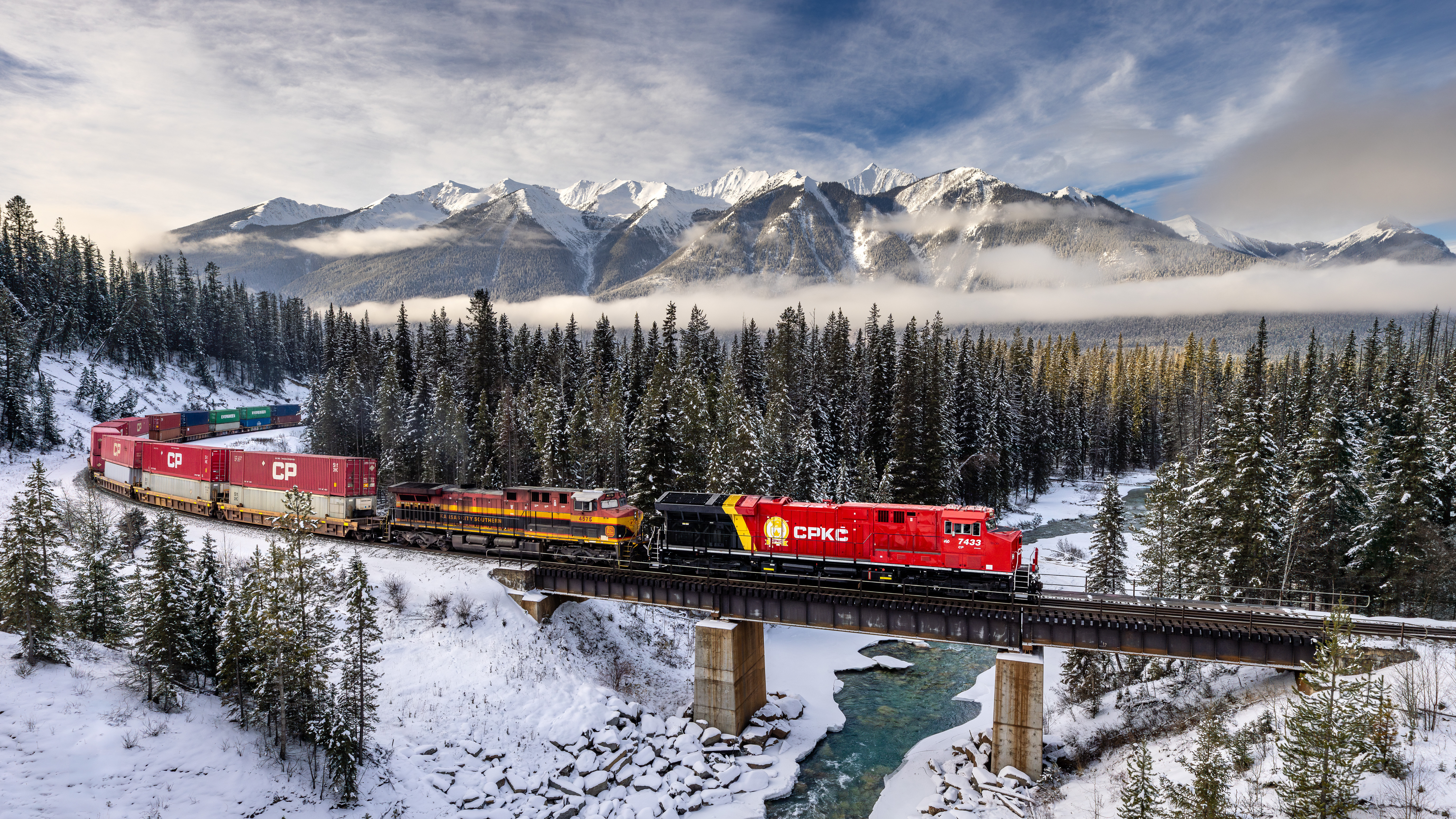 Train crossing a bridge in a snowy mountain landscape HD Wallpaper