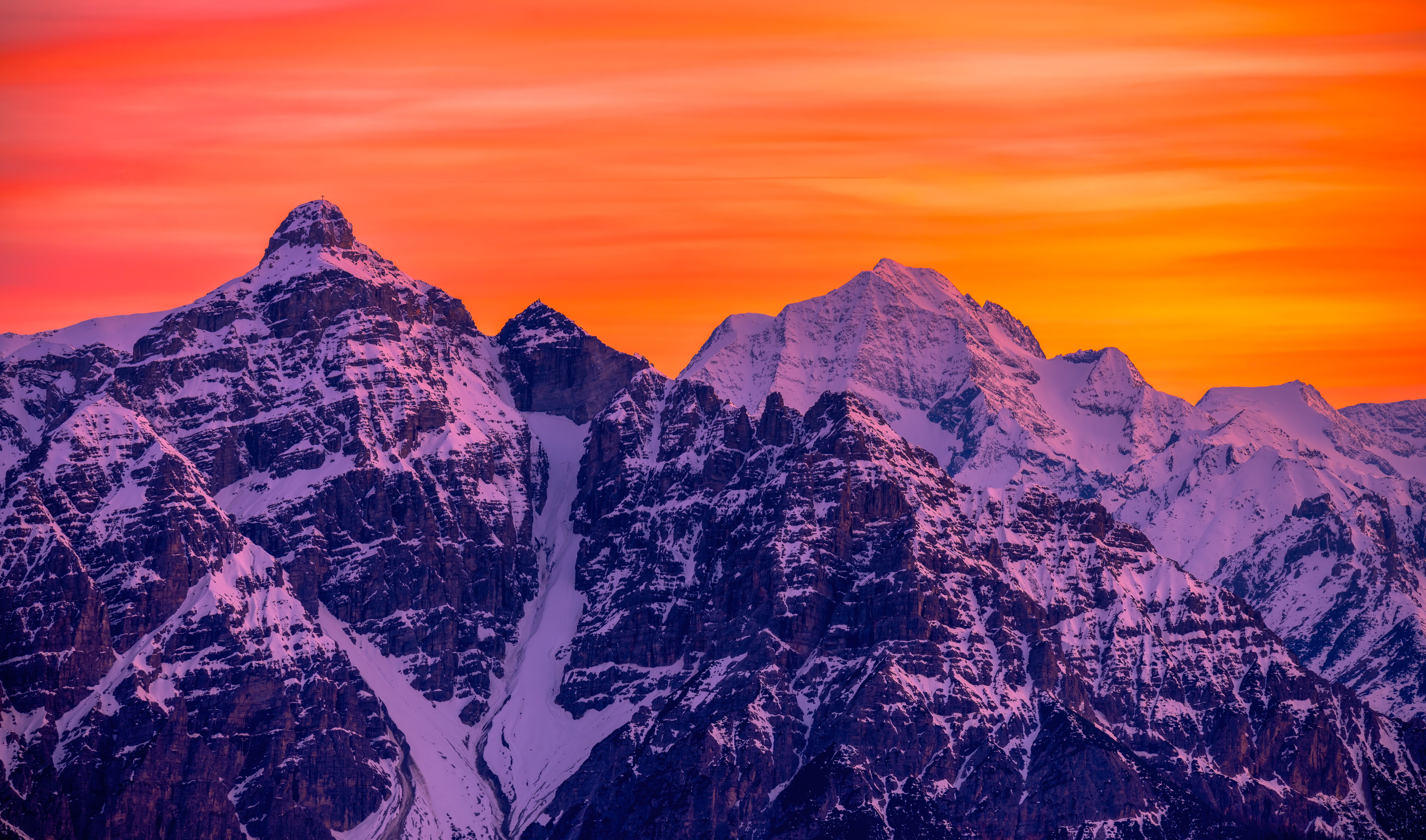 Snow-capped mountains under a vibrant orange sunset sky HD Wallpaper