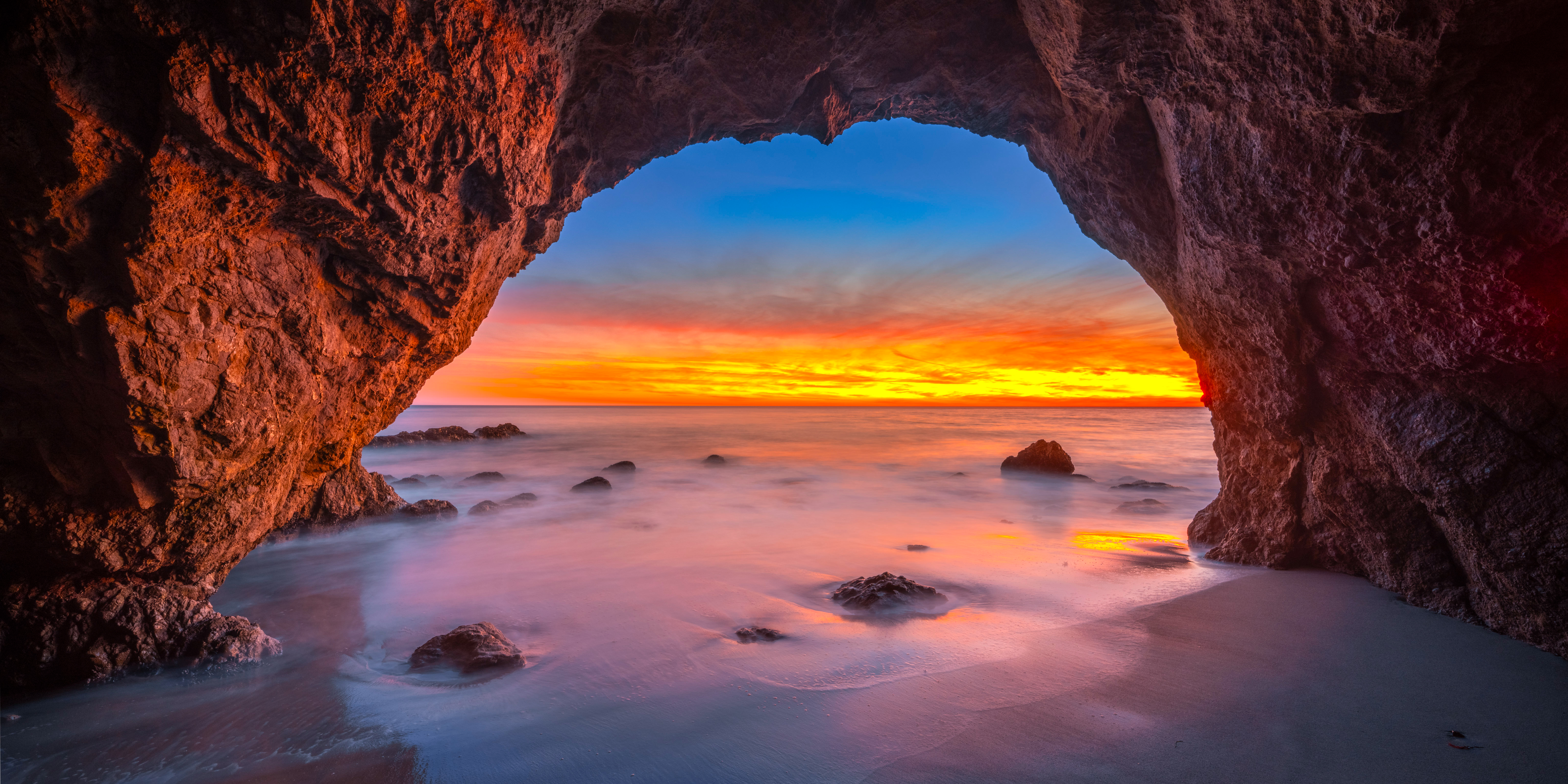Cave entrance overlooking ocean at sunset with long exposure HD Wallpaper