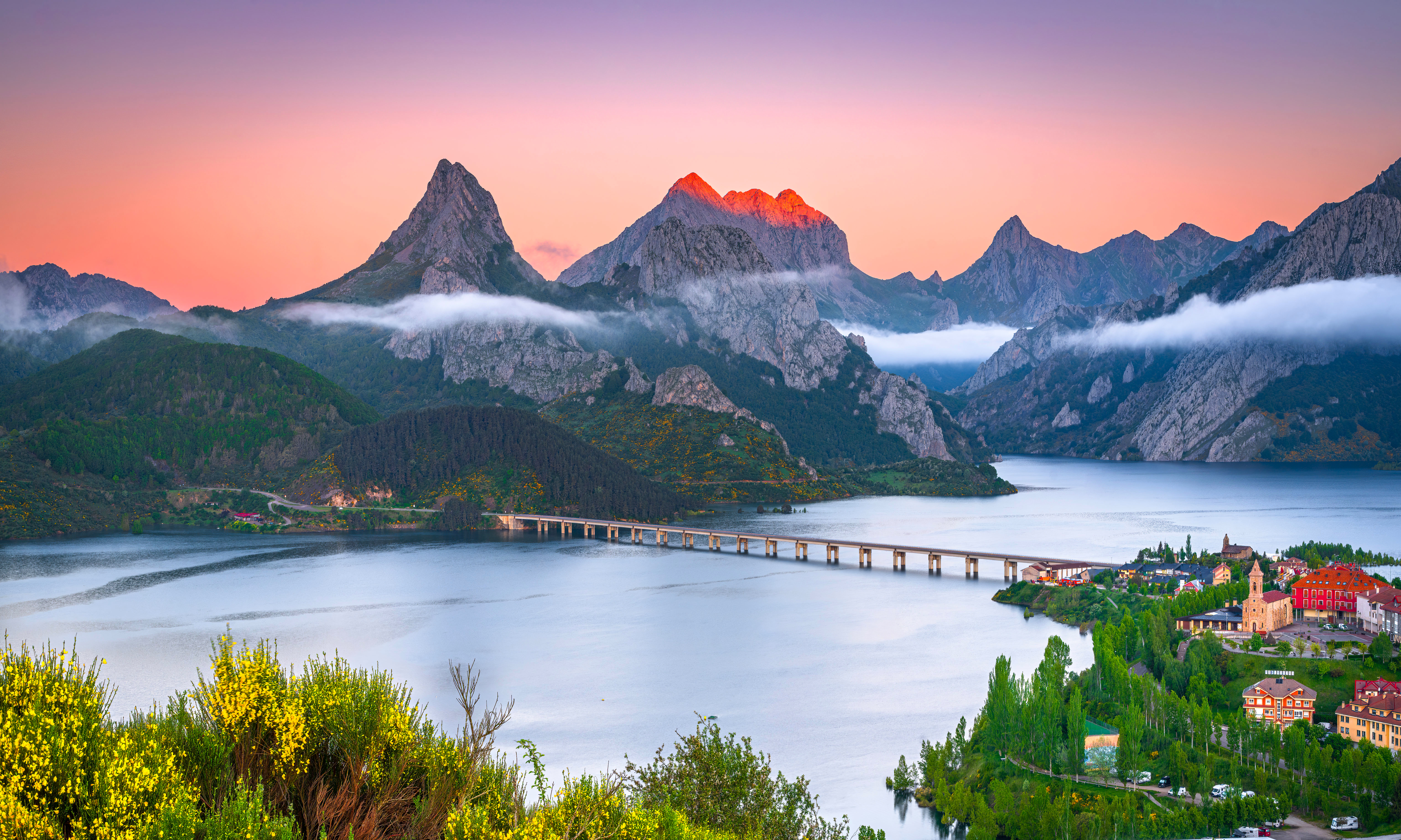 Mountains over a lake with a bridge and town HD Wallpaper