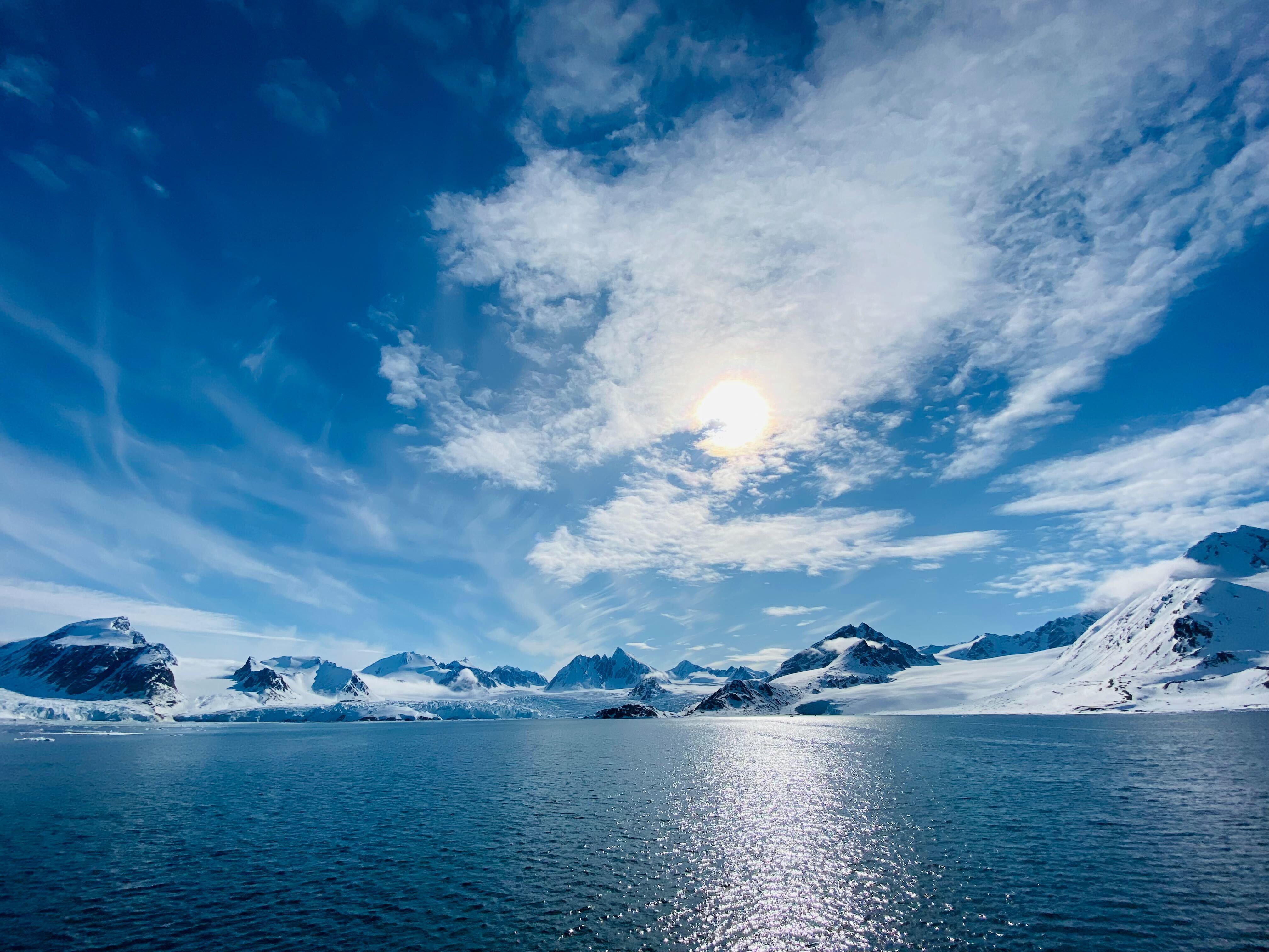 Snow-capped mountains and sea under a cloudy sky HD Wallpaper